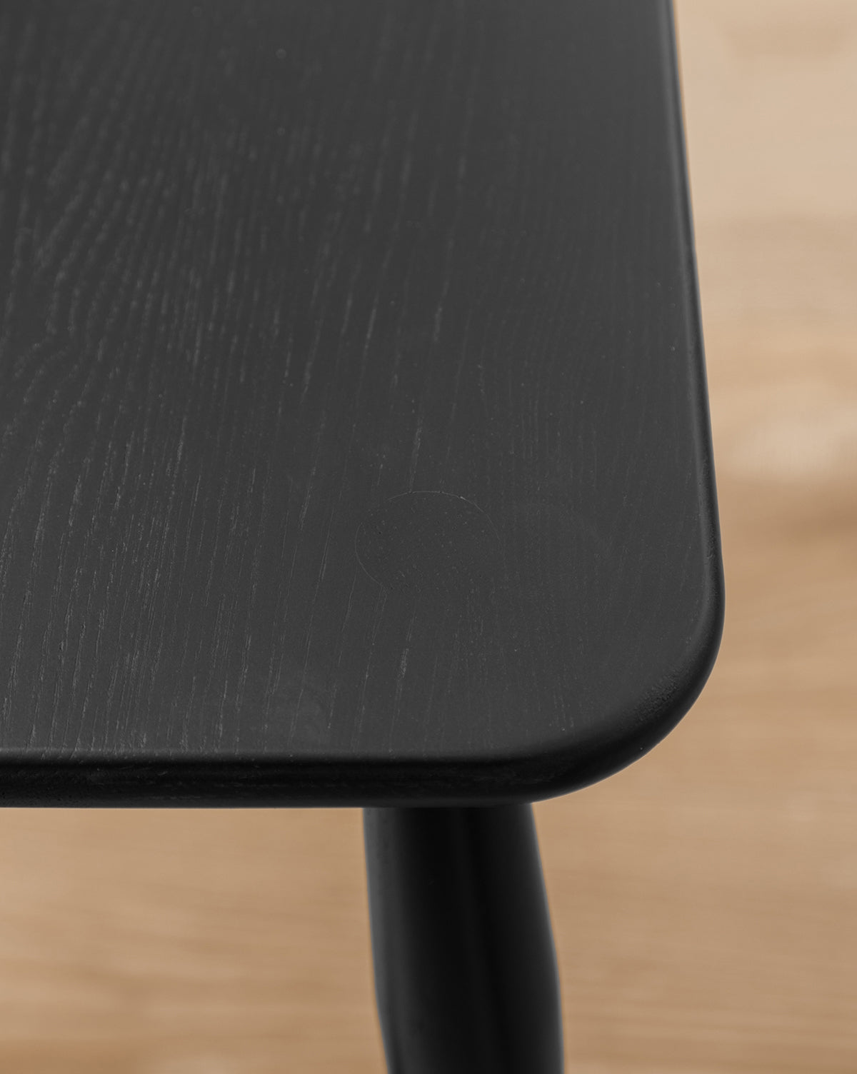 Featuring a close-up of a black wooden table with rounded edges and a matte finish, this piece adds sophistication to any dining area. For effortless style, pair your table with the elegant Whittaker Chair, by McGee & Co.