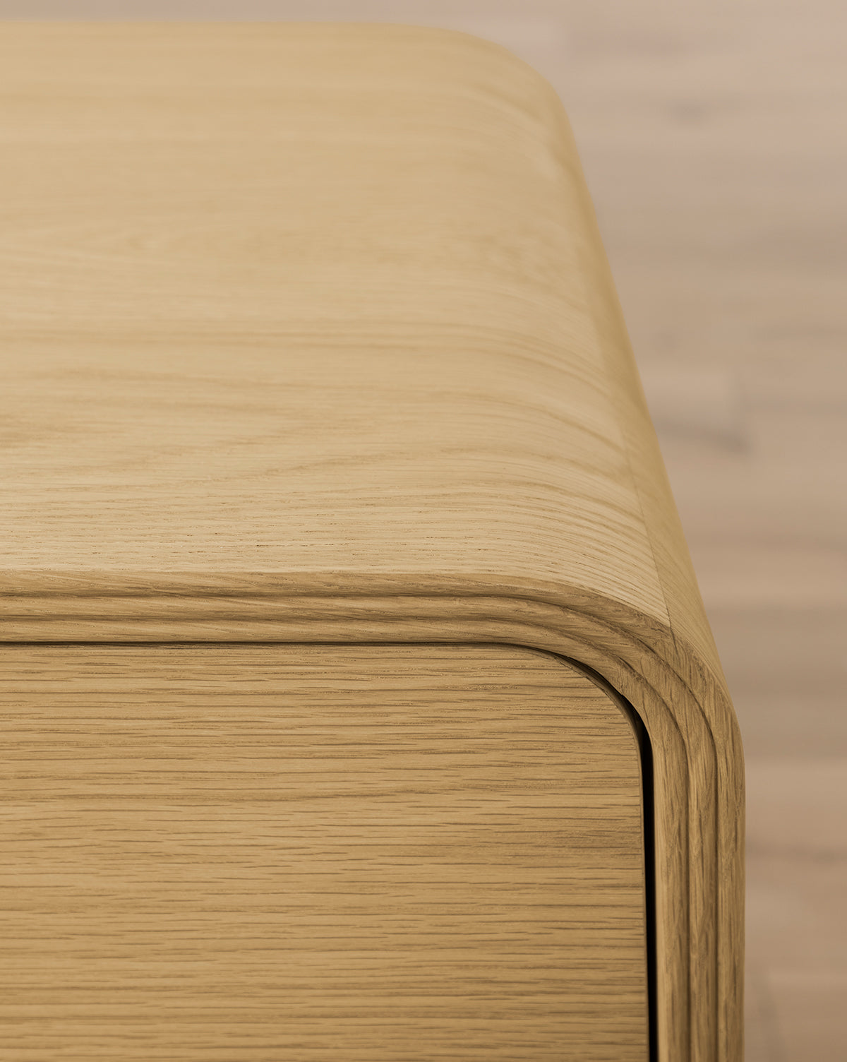 Close-up of the Wilkins Oak Nightstand, featuring smooth, rounded edges and prominent wood grain for an elegant touch to any bedroom décor, set against a softly blurred light background, by McGee & Co.