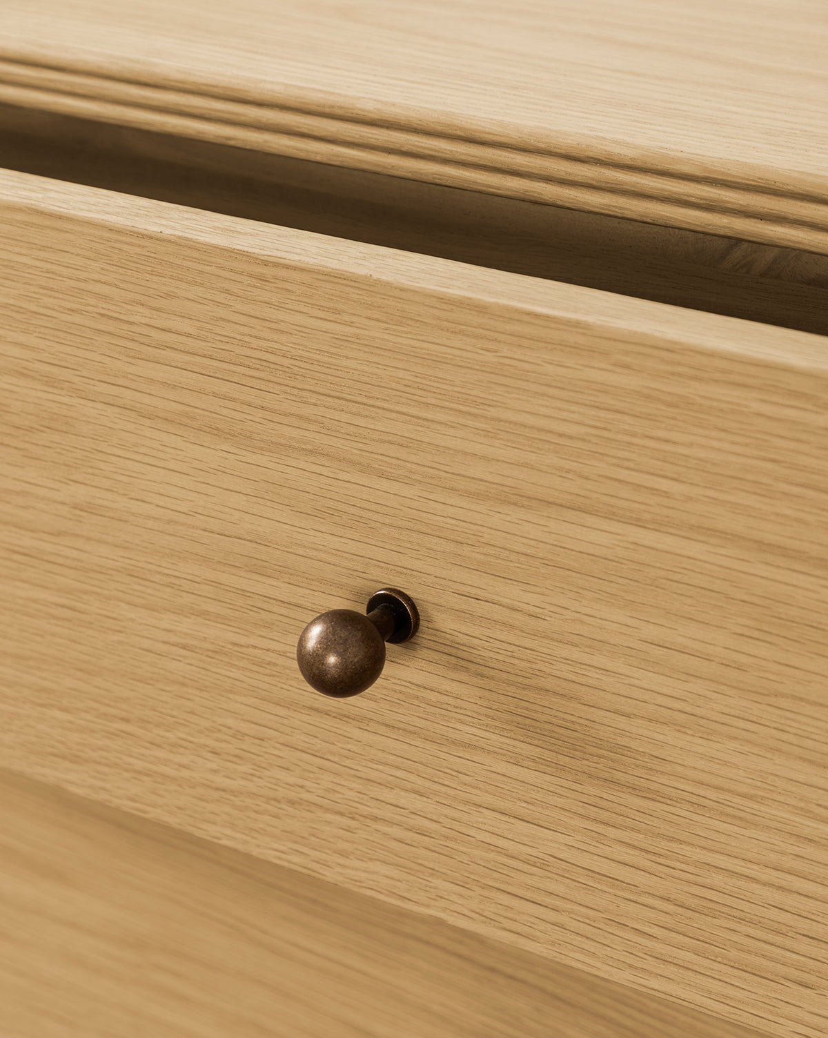 Close-up of a partially open Wilkins Oak Nightstand drawer, featuring a round bronze knob and light wood finish—ideal for enhancing your bedroom décor, by McGee & Co.