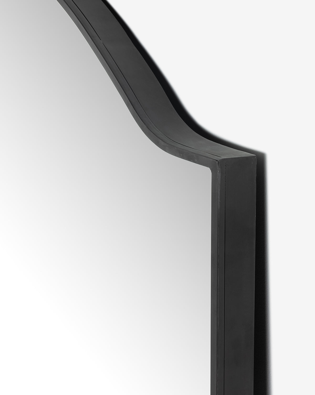 Close-up of the Willson Floor Mirror, featuring its arched top and black gunmetal frame, showing the left edge and part of the reflective surface against a plain white background, by McGee & Co.