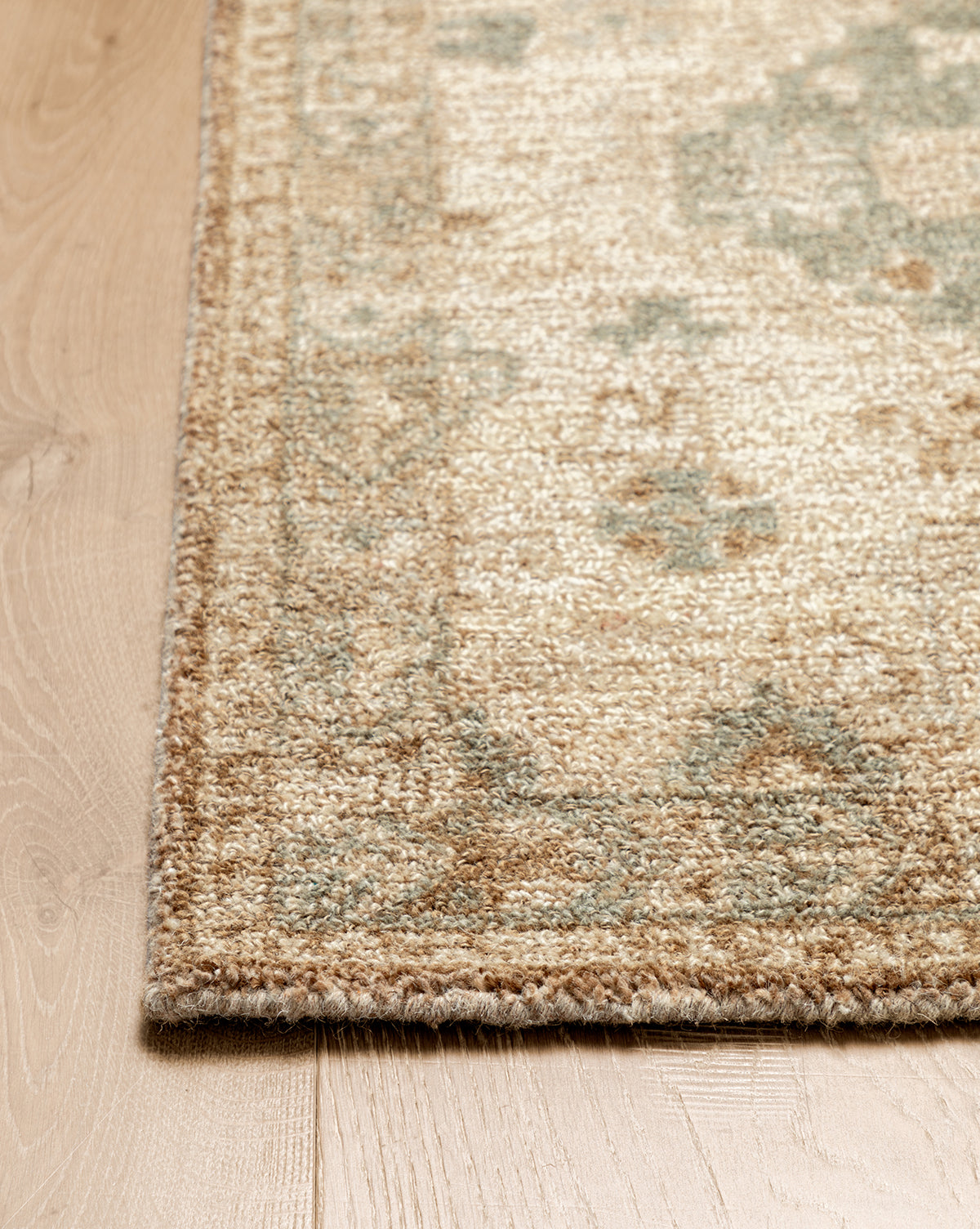 A close-up of the Wilshire Natural Hand-Tufted Wool Rug on a wooden floor highlights its intricate border, beige and light green pattern, textured wool surface, and spill-resistant qualities, by McGee & Co.