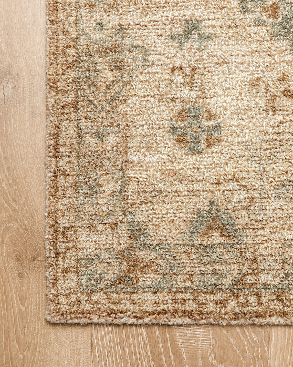 A close-up of the Wilshire Natural Hand-Tufted Wool Rug on a light wood floor highlights its subtle floral design, textured fibers, and spill-resistant surface for easy maintenance, by McGee & Co.