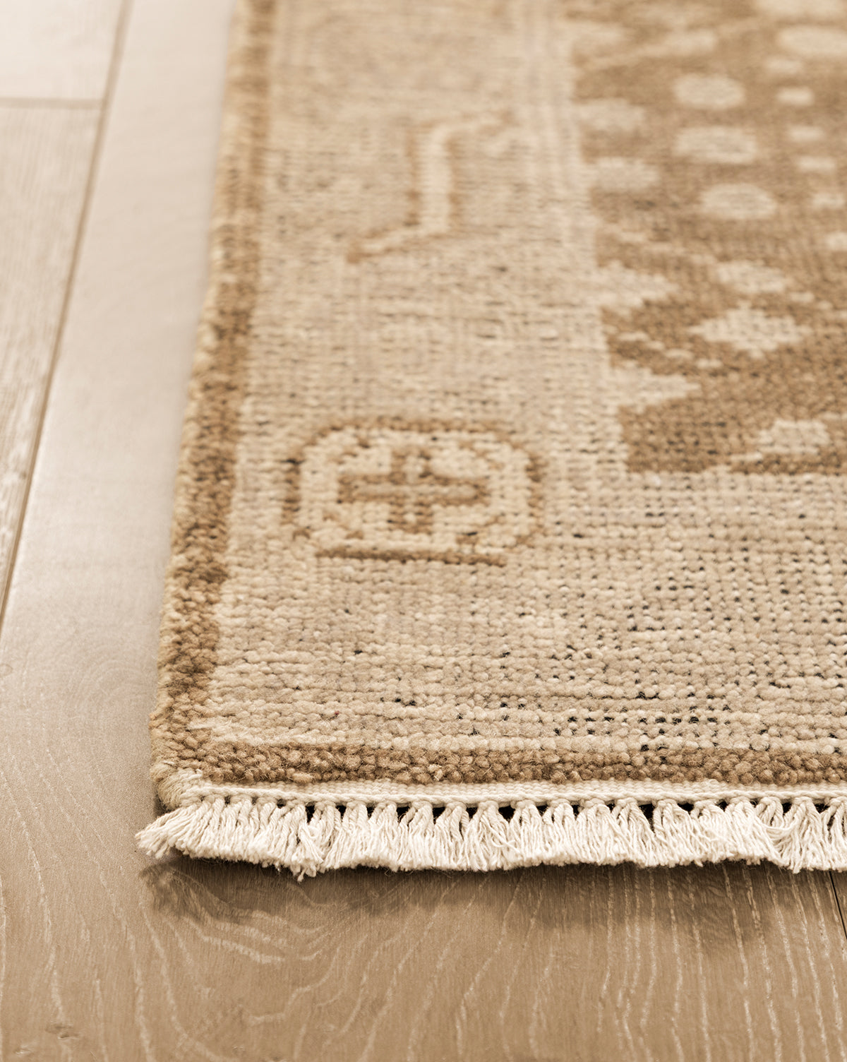 Close-up of the Windsor Hand-Knotted Wool Rug in beige, featuring geometric patterns and fringe along one edge on light wood flooring. The wool texture and intricate weave details are clearly visible, by McGee & Co.