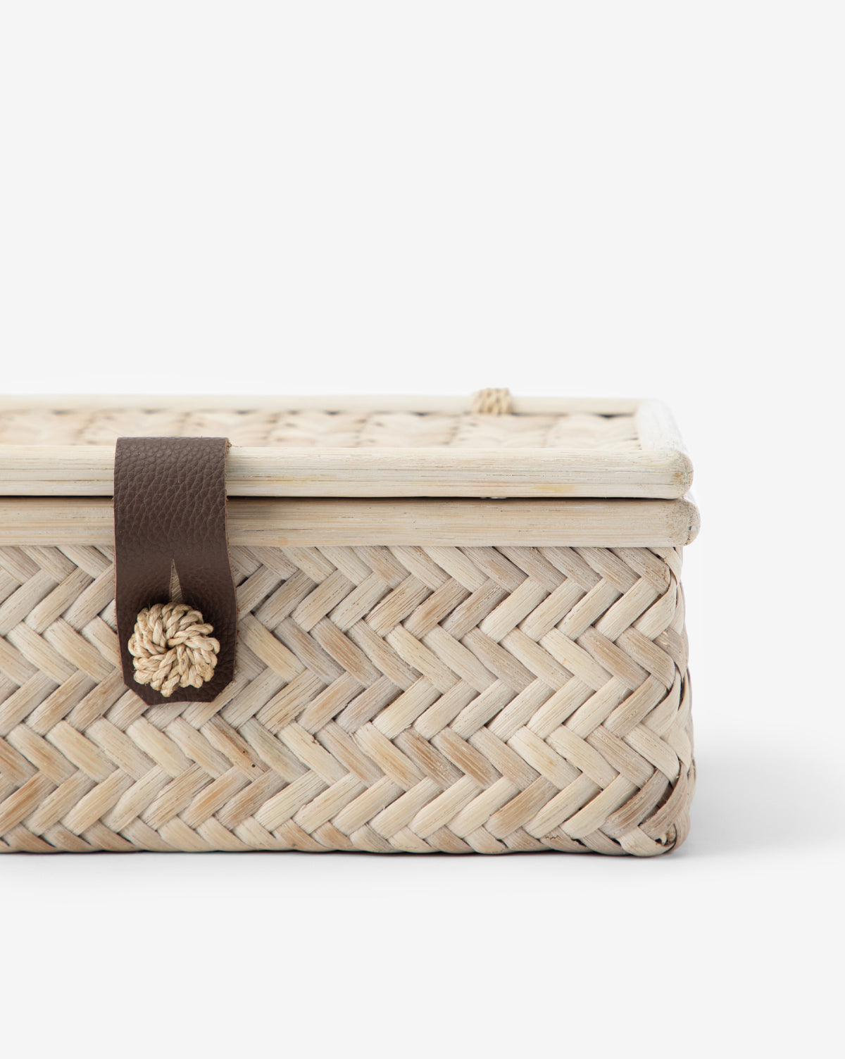 A close-up of the Winnie Wicker Box, a rectangular basket with a herringbone weave, fitted lid, and a brown leather latch adorned with a decorative knot for closure.
