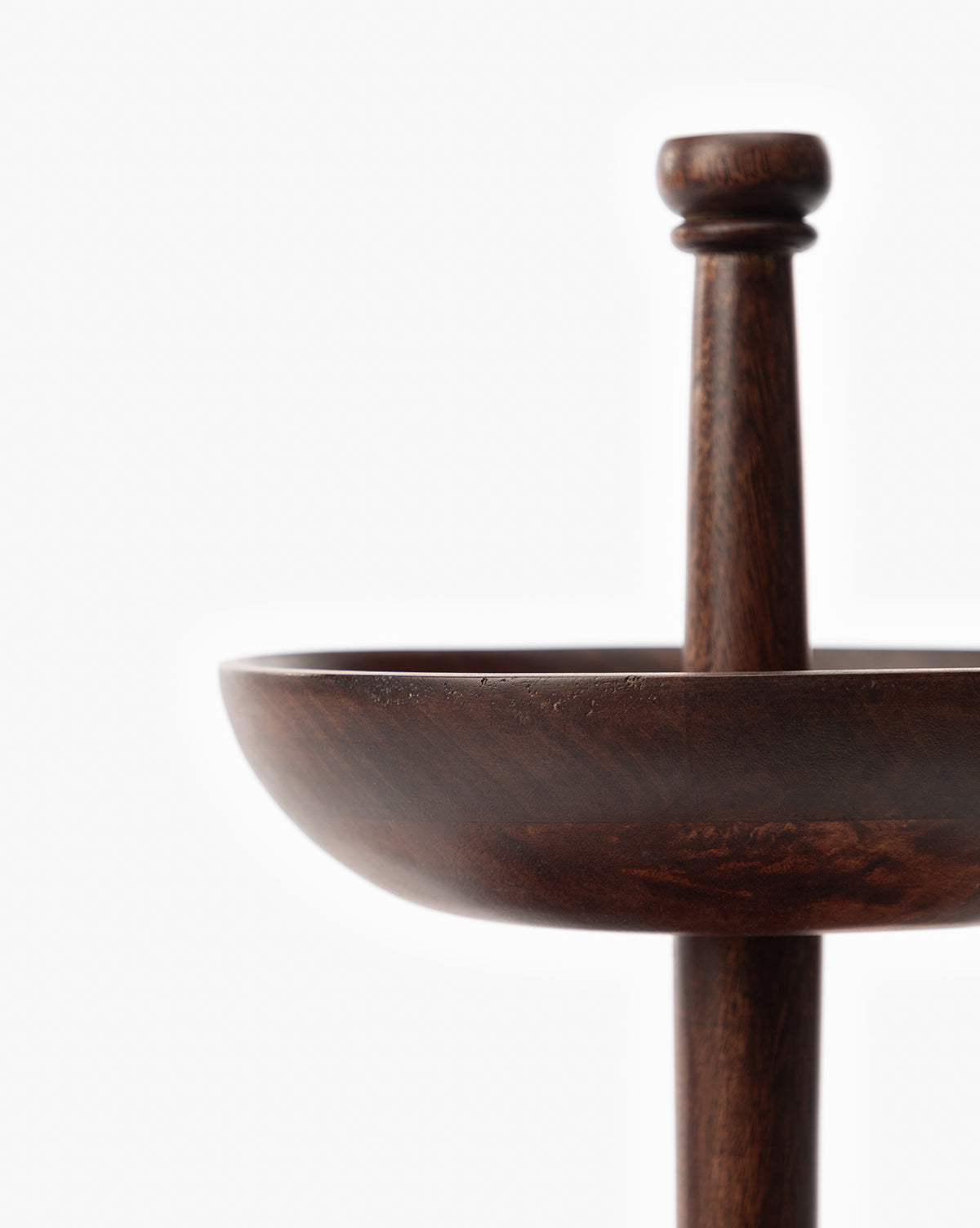 Close-up of the Winward Tiered Pedestal, a dark wood tray with a raised central handle, displayed against a plain white background. Only part of its sculpted design is visible, emphasizing minimalism, by McGee & Co.