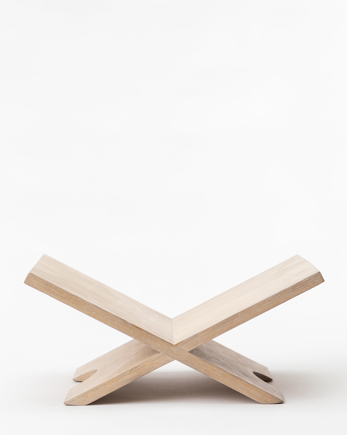 The Wooden Book Display features two interlocking light oak slats forming an X shape, creating a simple holder for books. It is shown against a plain white background.