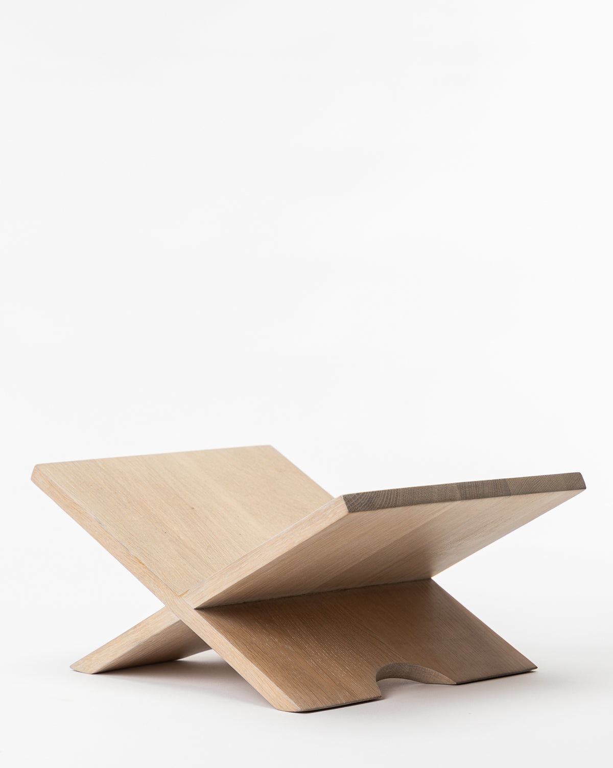 The Wooden Book Display, crafted from oak wood, features two flat panels that intersect to form an X shape, providing a sturdy and stylish surface for holding open books. It stands out beautifully against a plain white background.
