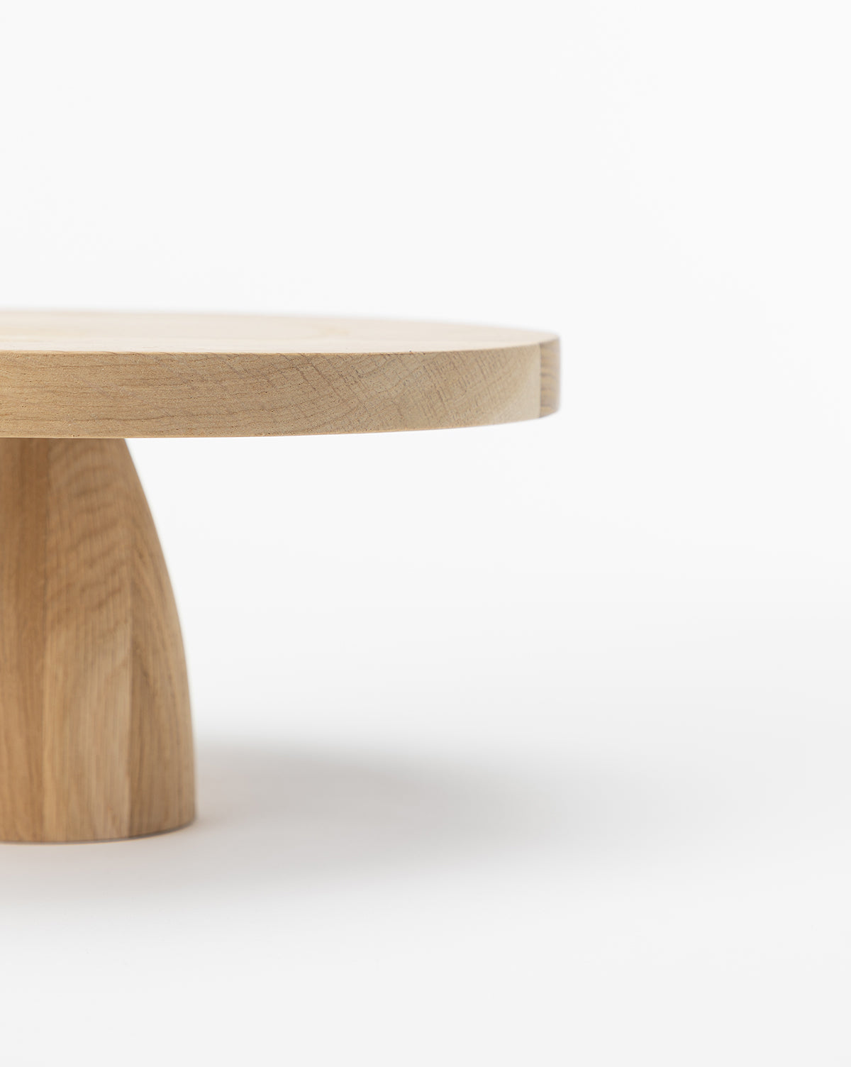 The Wooden Cake Stand features a minimalist design with a round top and sturdy base, shown partially against a plain white background, by McGee & Co.
