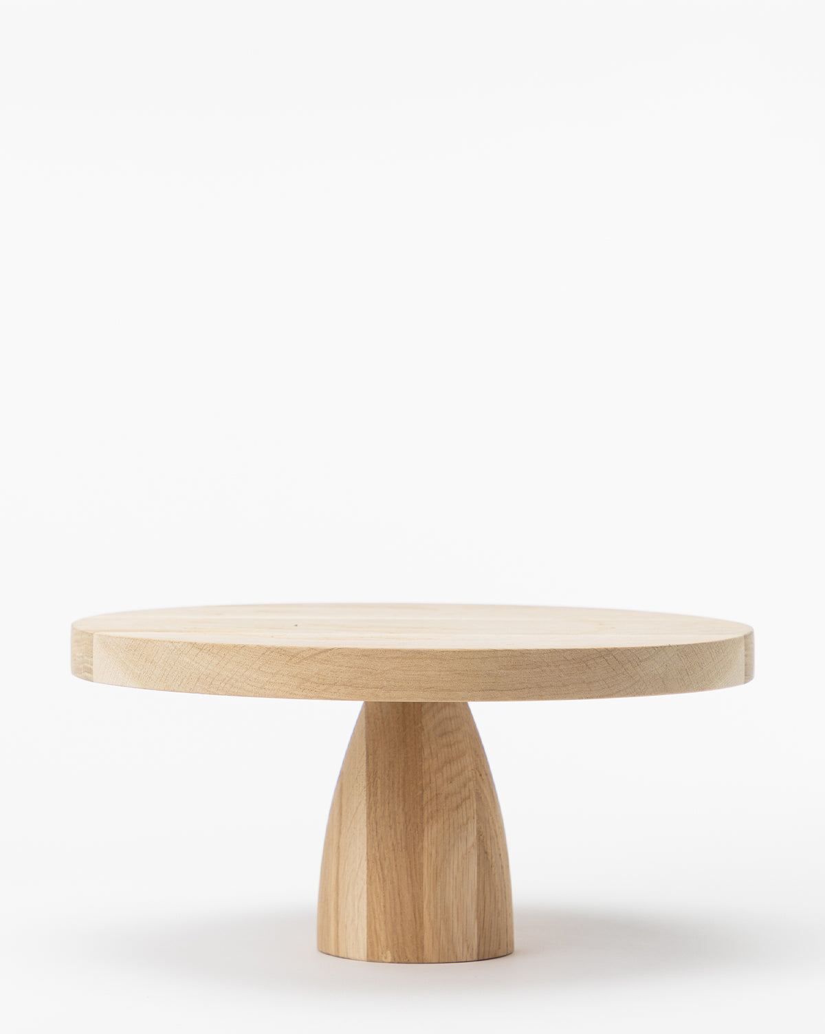 The Wooden Cake Stand features a round, light wood design with a thick top and sturdy, tapered base—ideal as a striking home decor piece or an oversized cake stand—shown on a plain white background, by McGee & Co.