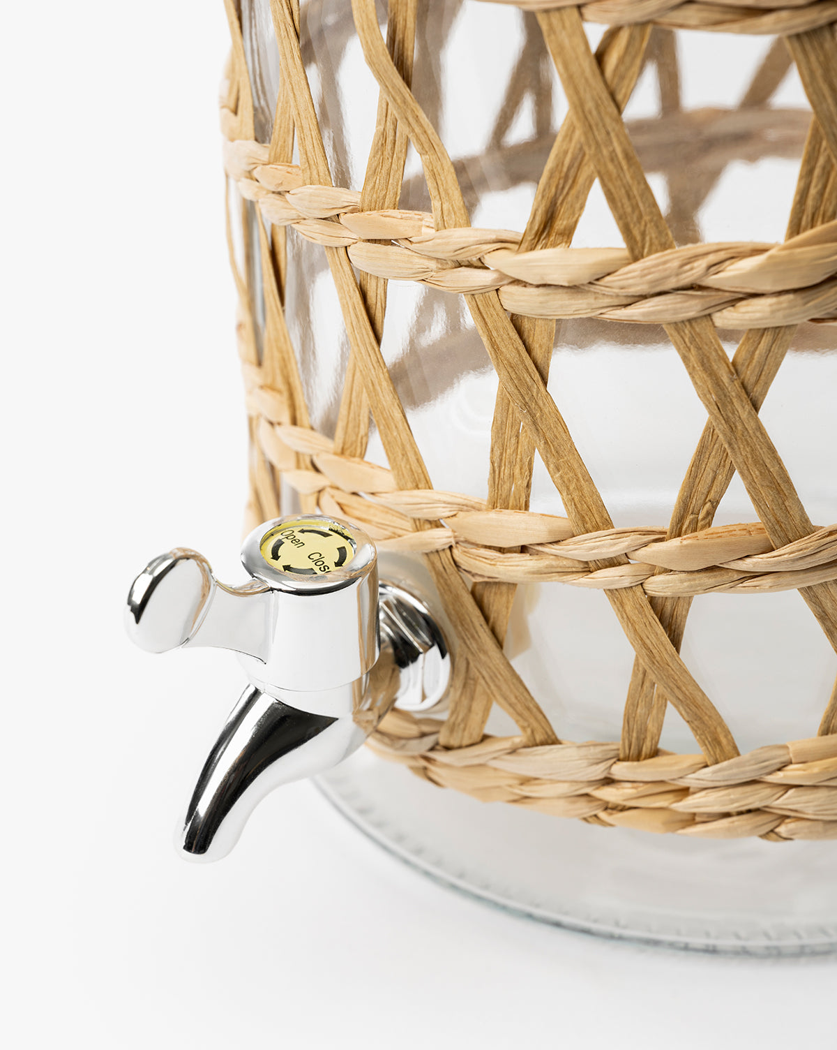 Close-up of the Glass Beverage Dispenser with Woven Sleeve, featuring a shiny silver spigot and a seagrass-wrapped design, set against a plain white background, by McGee & Co.