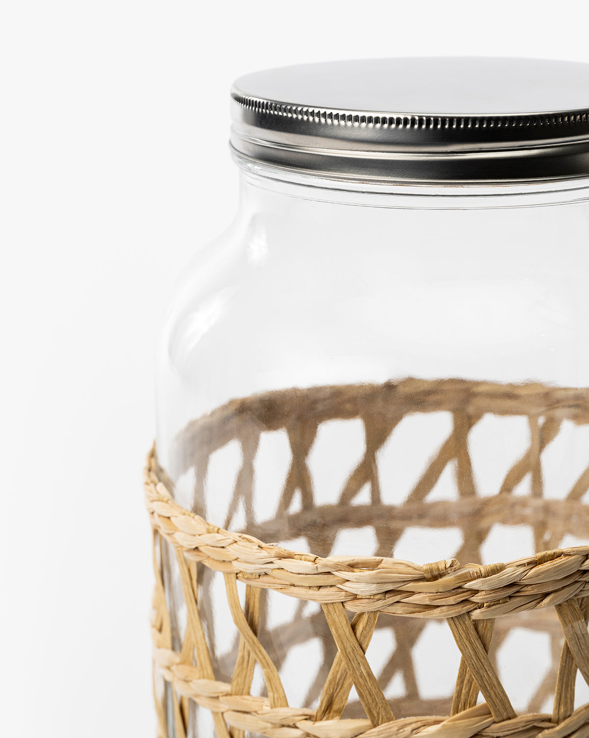 The Glass Beverage Dispenser with Woven Sleeve features a clear body, a silver screw-on lid, and a partially woven sleeve, shown against a plain white background, by McGee & Co.