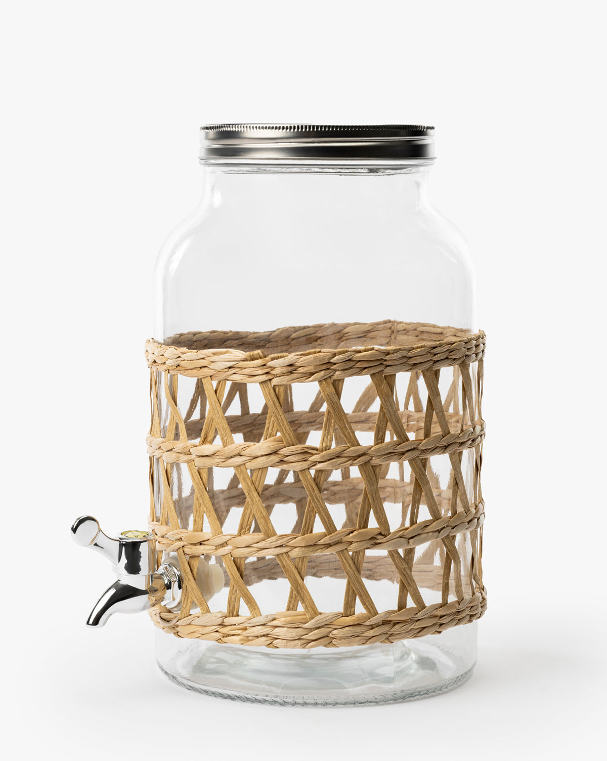 The Glass Beverage Dispenser with Woven Sleeve features a clear glass body, metal lid, spout, and a decorative woven sleeve around the middle, shown against a plain white background by McGee & Co.