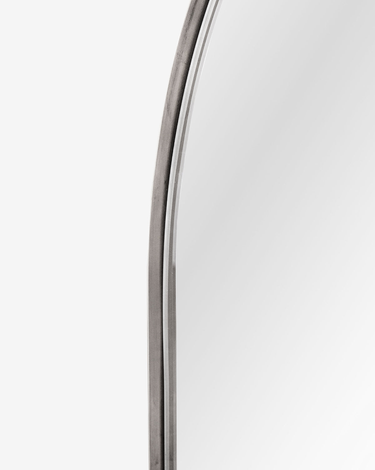 Close-up of the top left corner of the Wylie Arched Mirror, featuring a rounded metal frame and shatterproof glass, set against a plain white background, by McGee & Co.