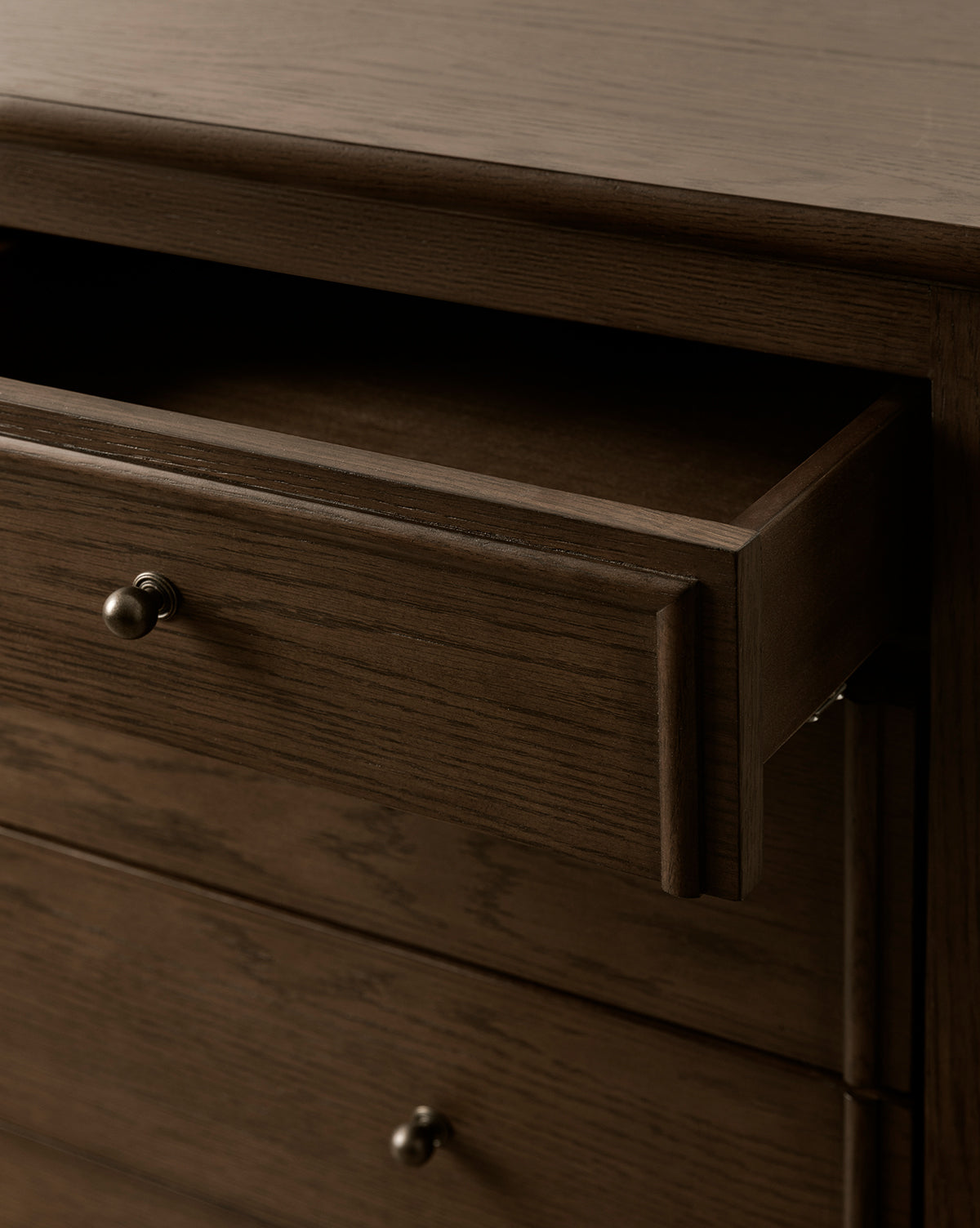 A close-up of the Yorkshire Dresser showcases its English oak finish and metal knobs. The partially open top drawer reveals spacious bedroom storage inside, by McGee & Co.