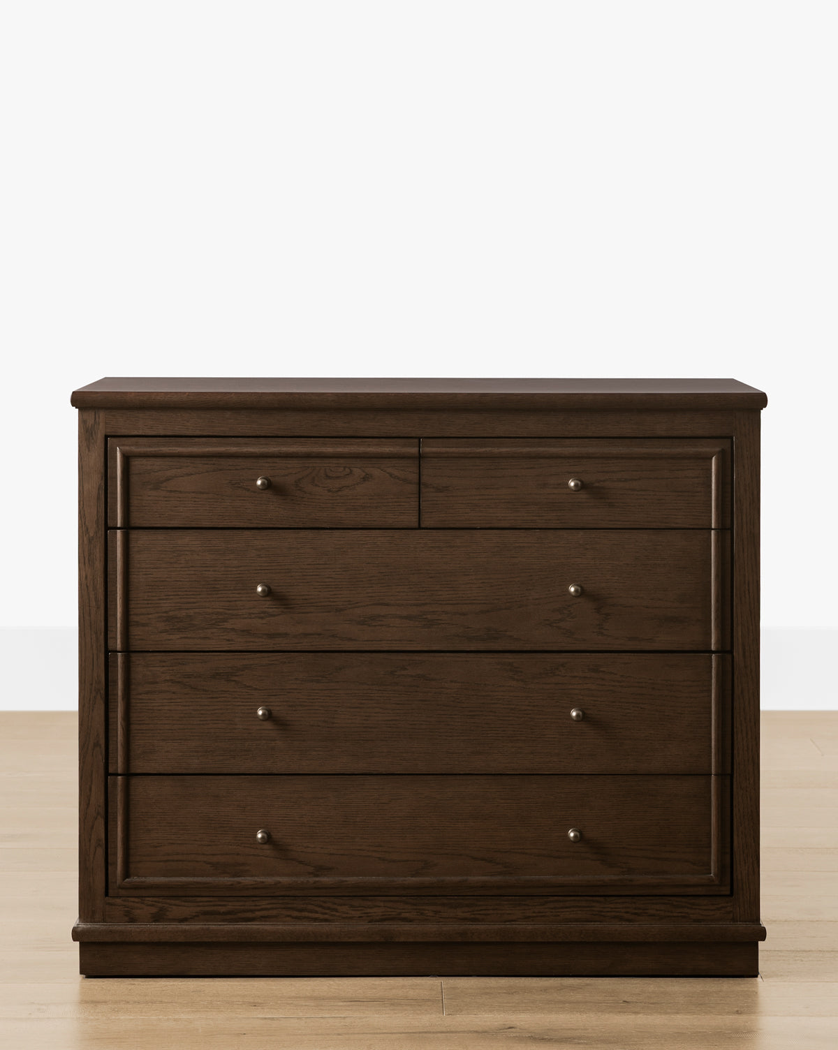 The Yorkshire Dresser, in dark brown with an English oak finish, offers elegant bedroom storage with six drawers—two small above four large—adorned with silver knobs, displayed on a light wood floor against a white background, by McGee & Co.