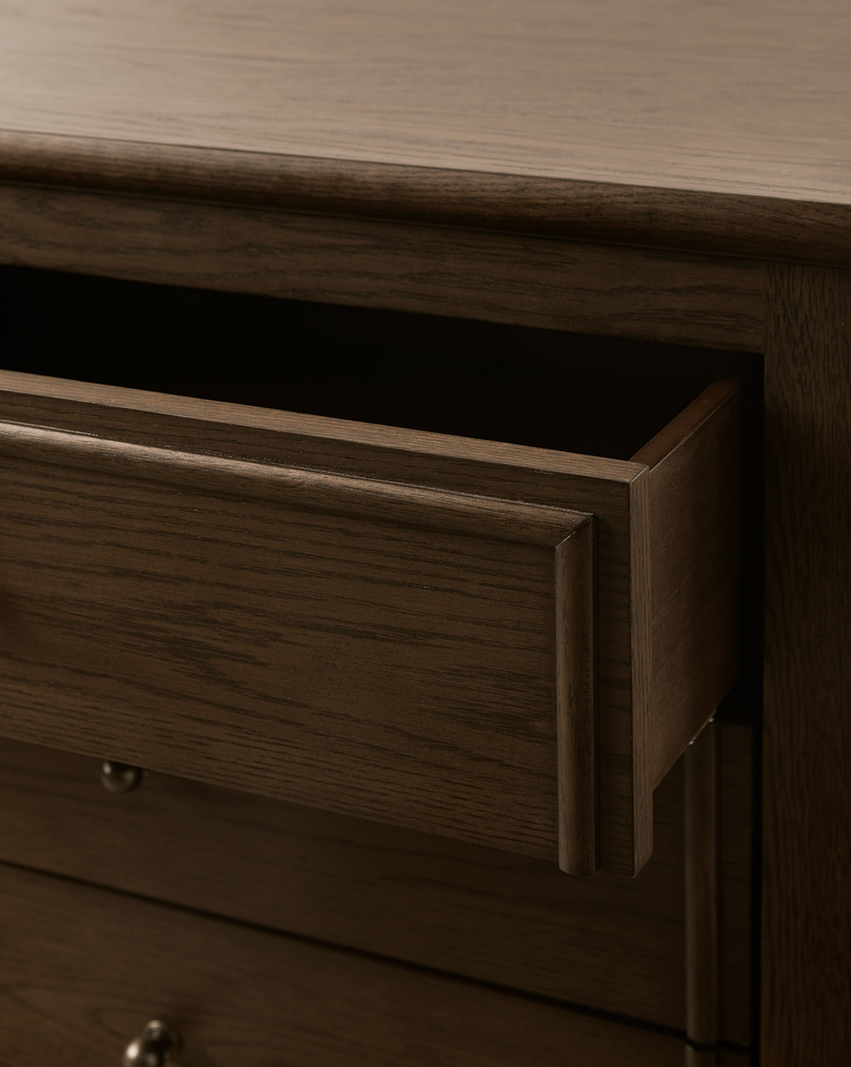 A close-up of the Yorkshire Nightstand with one drawer partially open, showcasing the smooth, dark wood grain and antique brass pulls on the lower drawers, by McGee & Co.