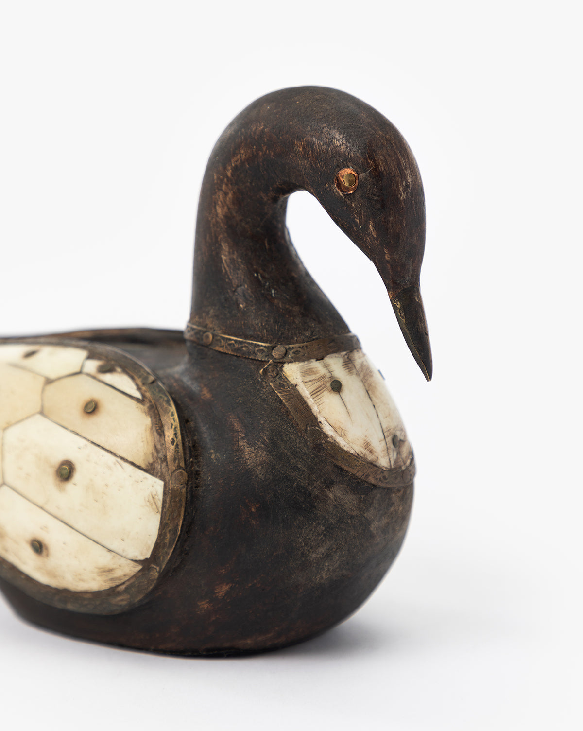 The Zella Swan Object is a vintage-inspired carved wooden swan with bone inlay panels on its chest and side, visible metal studs, and a plain white background—a unique decorative piece that adds charm to any space.