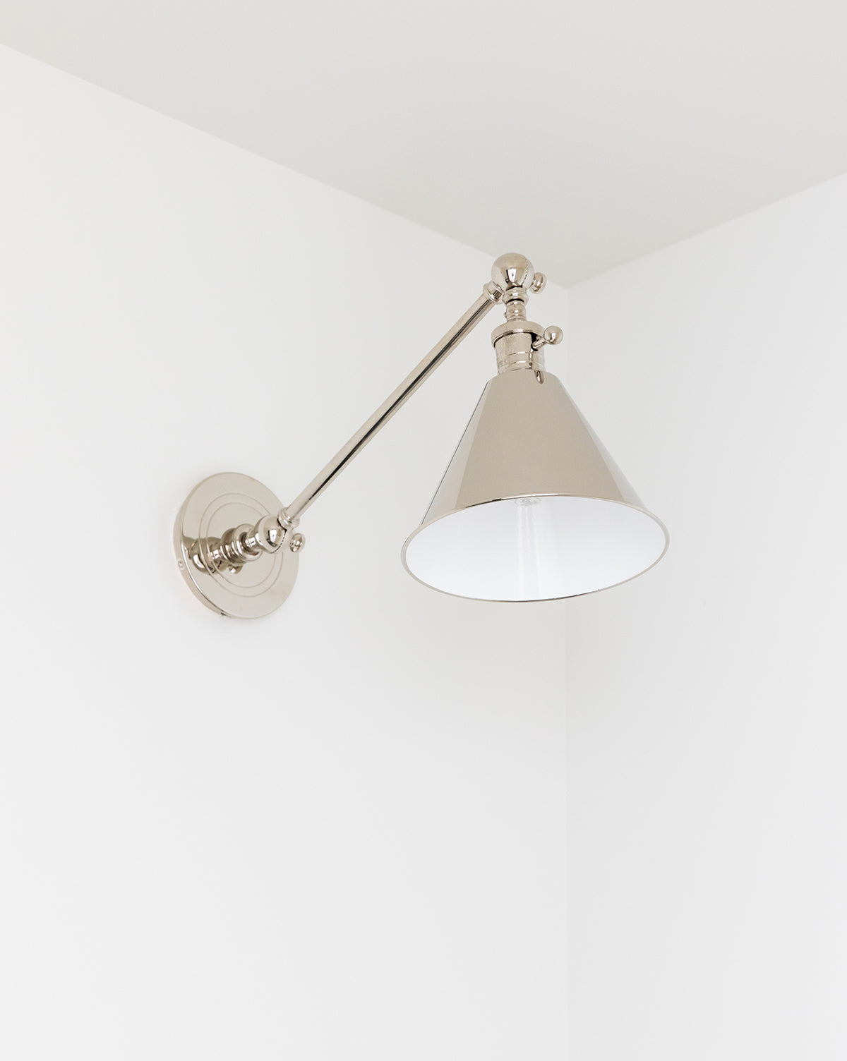 The Boston Single Arm Library Light by Visual Comfort & Co. Signature, with its modern metallic design and conical shade, is mounted on a white wall in the corner, complementing the room’s minimalist decor. McGee & Co.