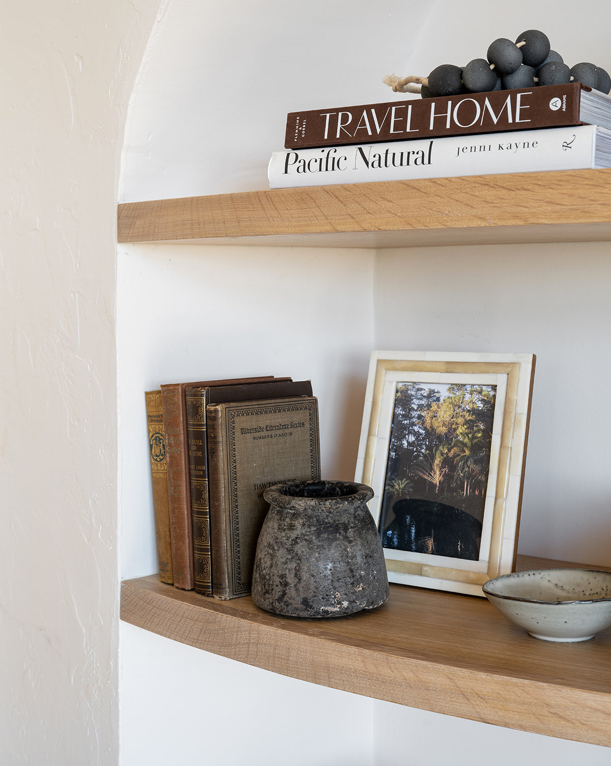 Wooden shelves showcase stacked books, a framed photo in the Inlay Bone Frame, vintage books, a rustic black vase, and a small ceramic bowl, creating a cozy and thoughtfully curated display.