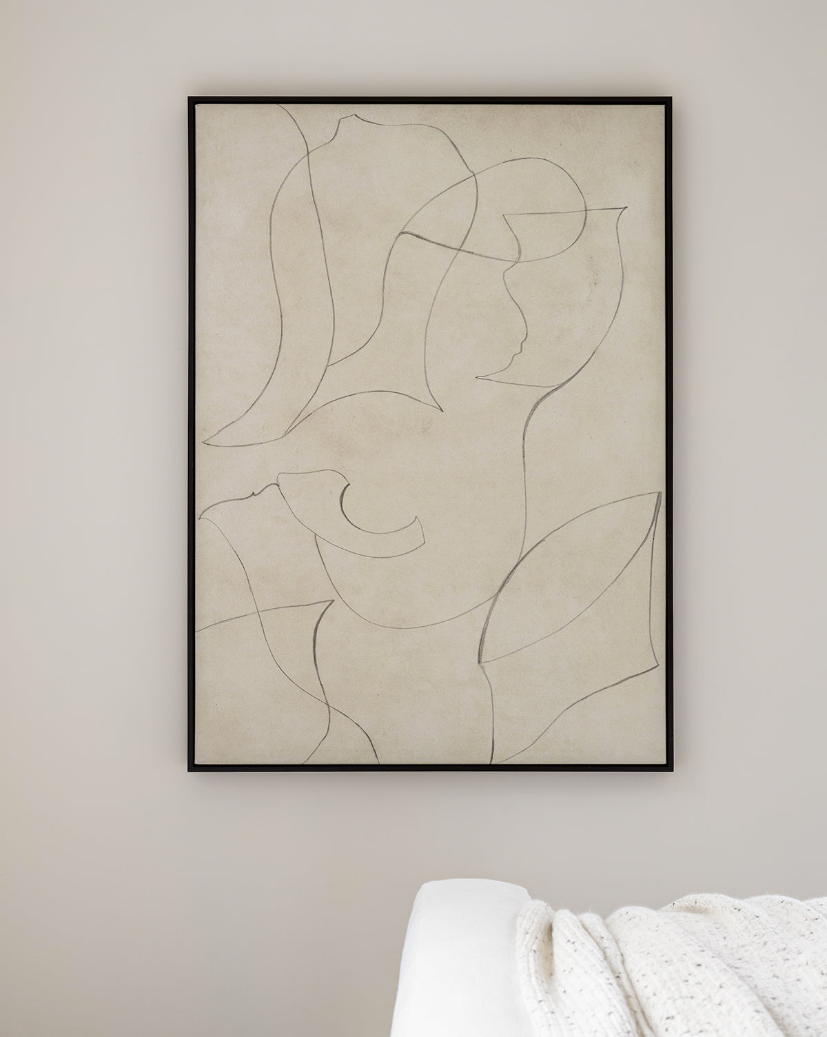 Sketched Thoughts—a minimalist abstract canvas in a black frame, featuring line art of human and organic shapes on a beige wall. In the lower right, a bed corner draped with a white knitted blanket adds cozy texture.