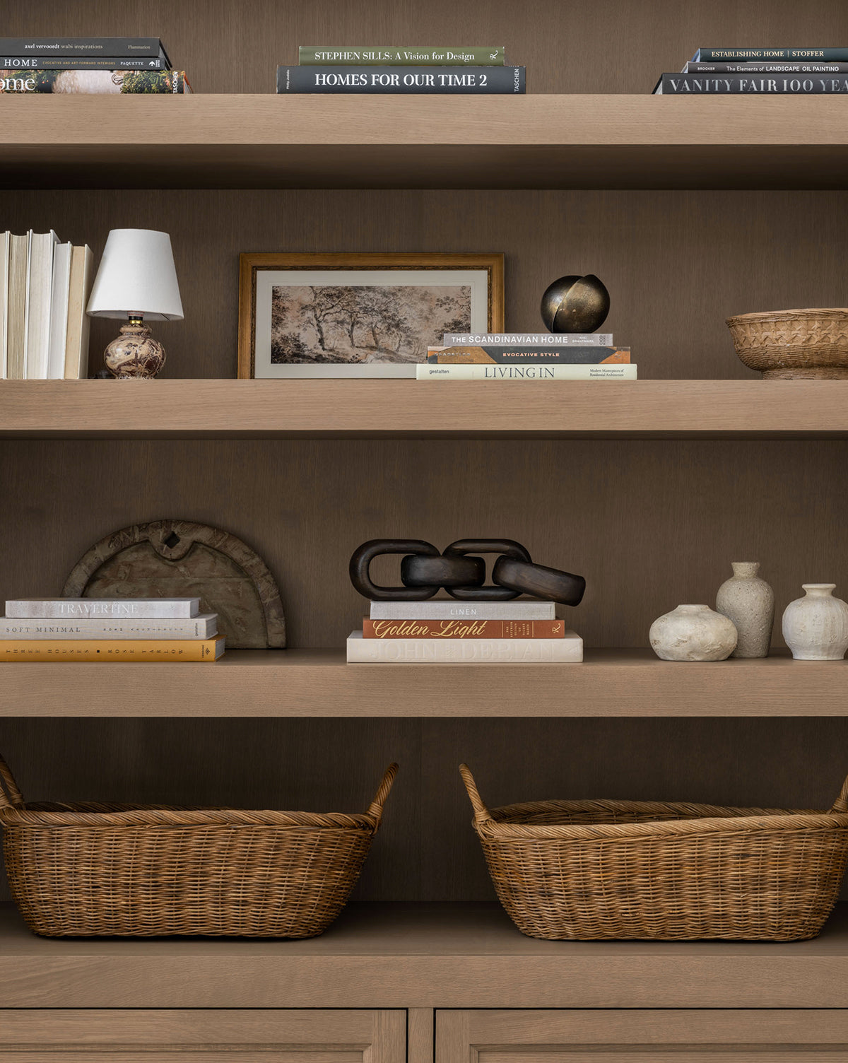 The Jackson Offset Sphere, styled with stacked books, decorative objects, small vases, baskets, a brass-finish lamp, framed art, and sculptural pieces on three wooden shelves, brings modern elegance to any room.