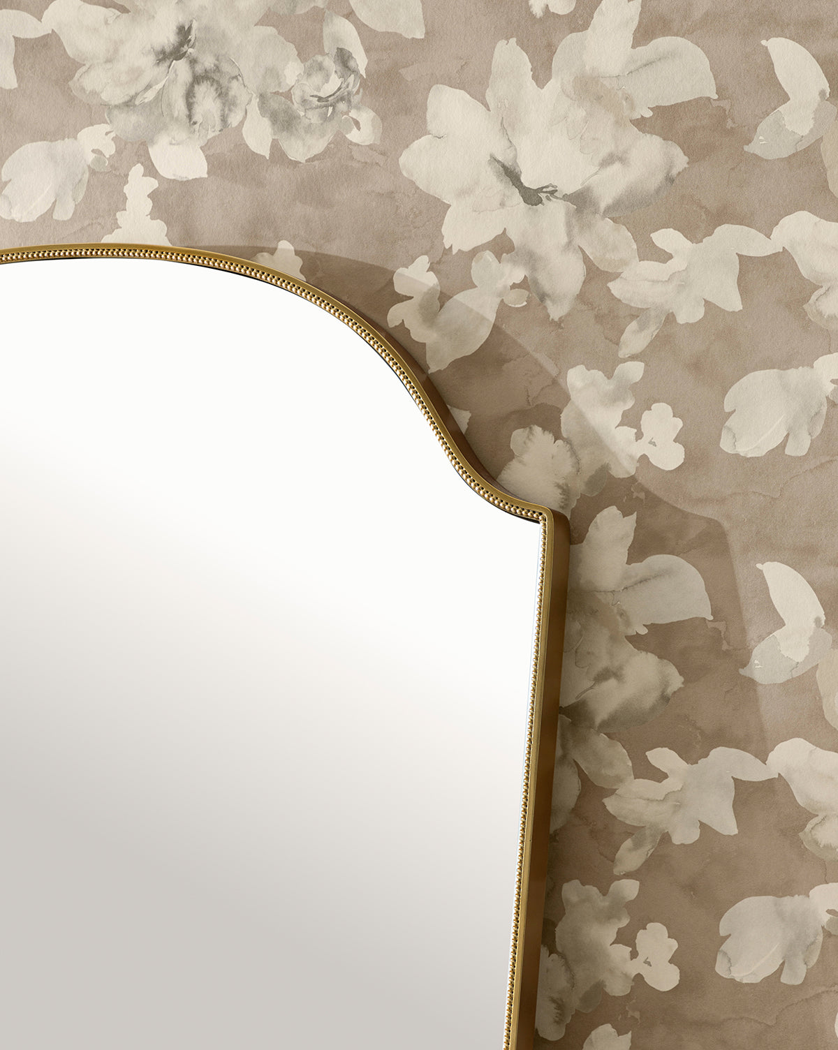 A curved mirror with a gold frame is partially visible against a beige wall decorated with Fiorella Wallpaper, which features an elegant white floral motif.