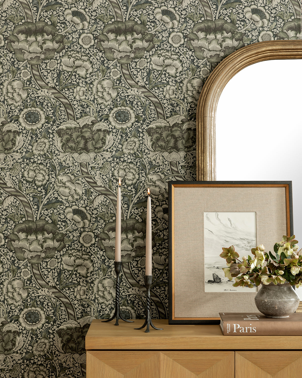 The dresser features two lit candles, a Paris book, and a vase of flowers beneath a mirror and floral wallpaper. The July in Kalamata giclee print in a distressed black frame completes this charming vignette.