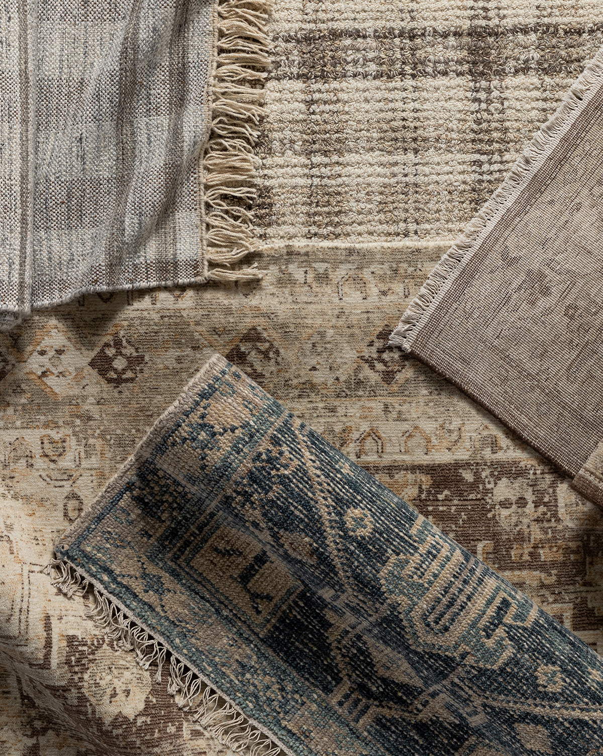 A top-down view of four overlapping Marcella Handwoven Rugs in neutral and blue tones, featuring unique patterns and fringed edges, including a wool blend and a neutral tan option, all arranged on a textured surface, by McGee & Co.