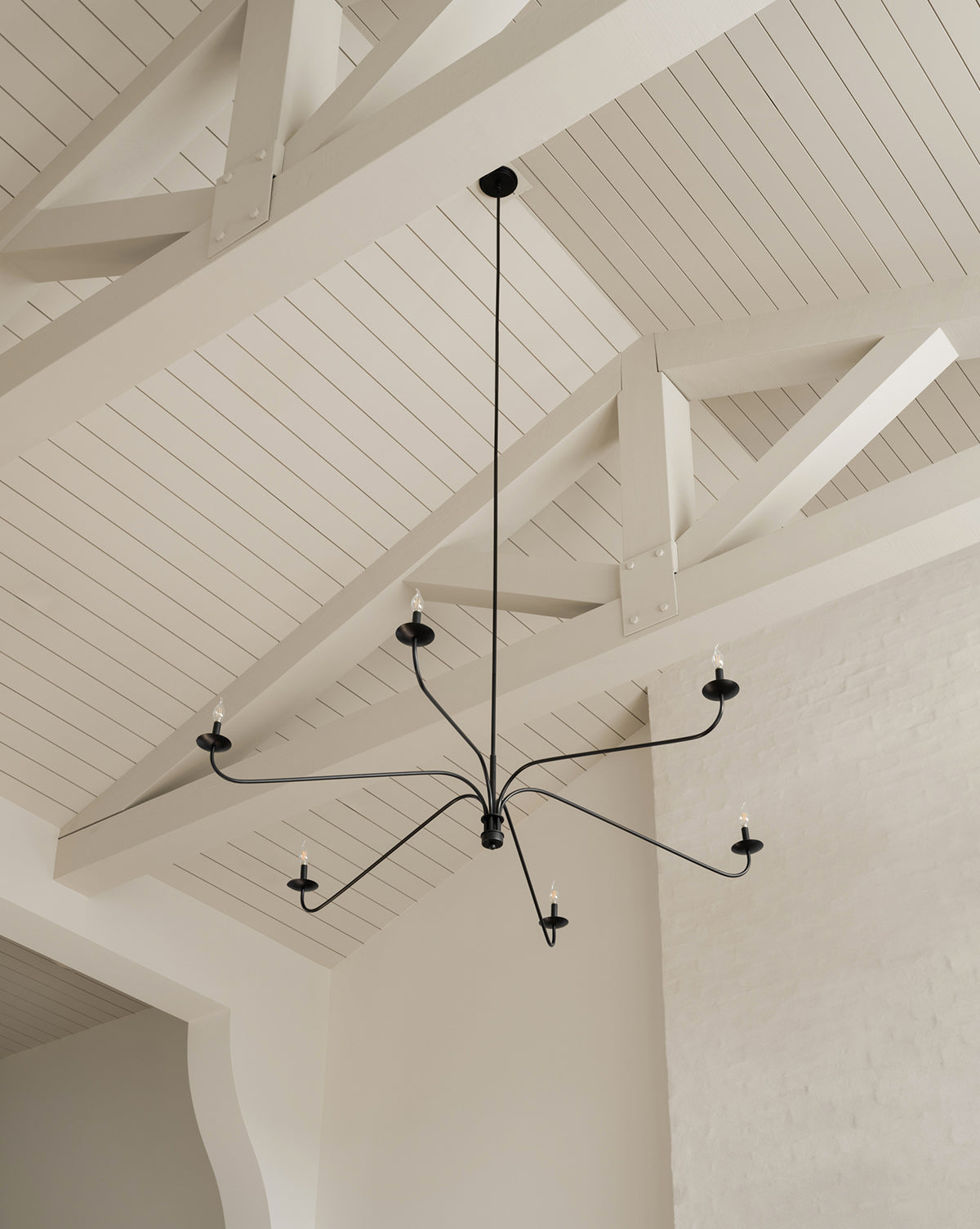 The Makerspalm Philomena Chandelier features six candle-style lights and blends classic and modern design, making it a striking addition to bright, airy rooms with high, white, vaulted ceilings and exposed beams by McGee & Co.