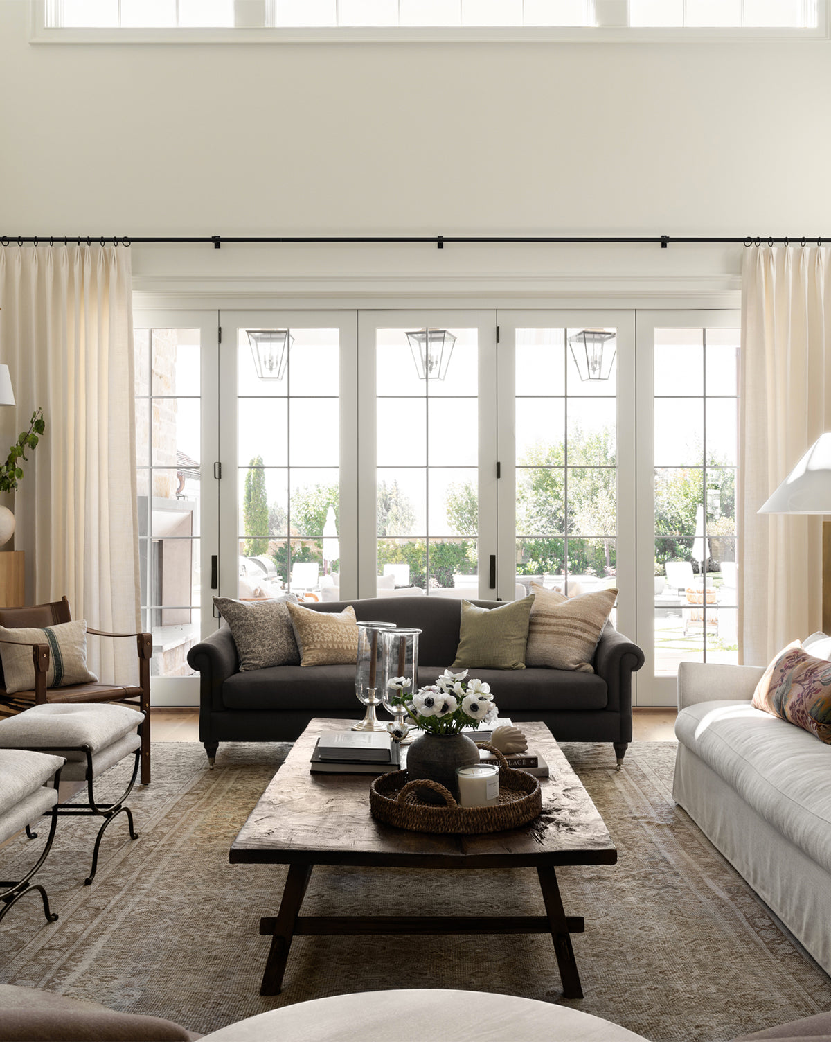 Bright living room with large windows, the customizable Hildegard Sofa 90 in neutral tones, a rustic wooden coffee table with decor, light curtains, and garden patio views. Natural light fills the space, making it warm and inviting by McGee & Co.