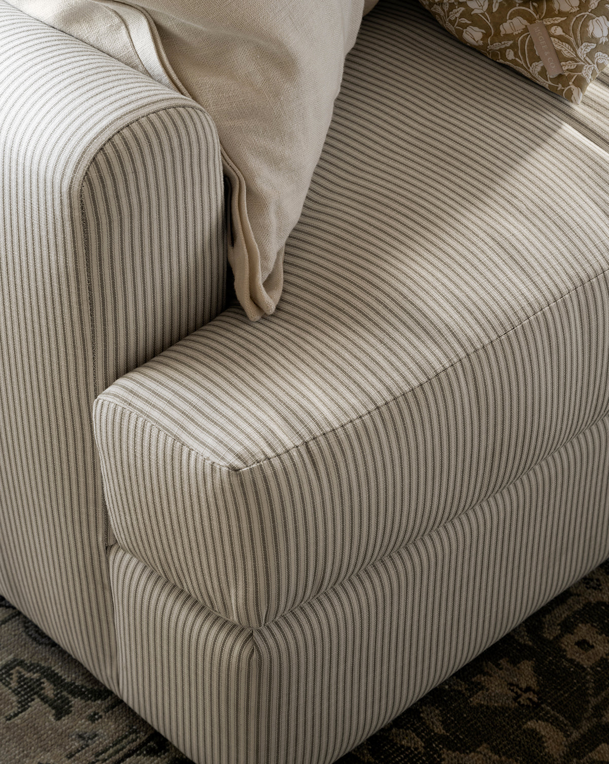 Close-up of the Winthrop Sofa 90 in beige and gray stripes, featuring a light cream pillow and a floral-patterned pillow on the armrest, set beside a dark patterned rug, by McGee & Co.