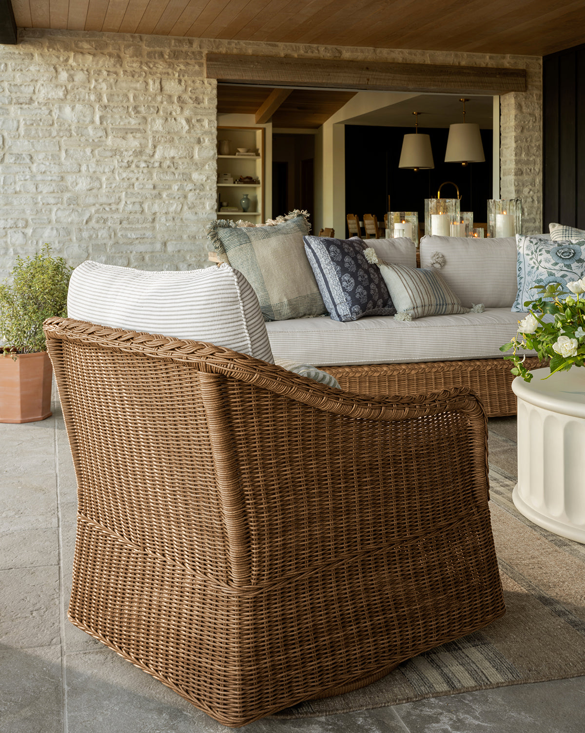 The Haviland Outdoor Swivel Lounge Chair with cushion is on a patio facing a beige sofa with throw pillows, near a white round coffee table and a potted plant by McGee & Co.