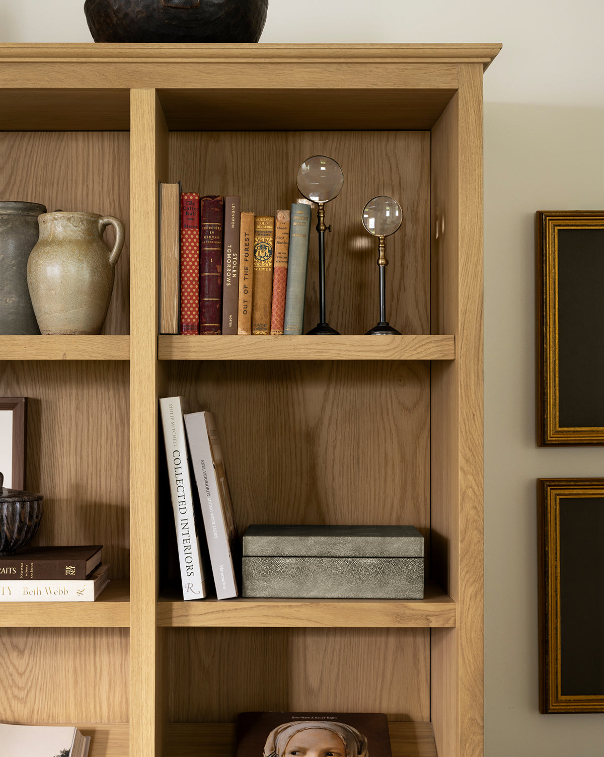 A wooden bookshelf showcases ceramic vases, a row of books, the Barnabas Standing Object, a decorative box, and partly visible framed pictures—perfect for curated home decor, by McGee & Co.
