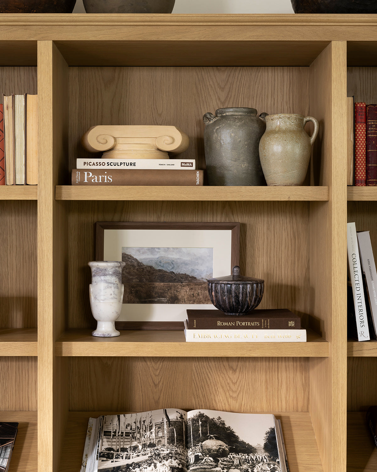 Wooden bookshelf with ceramic vases, decor pieces, and art books like Paris and Picasso Sculpture, featuring Marshland giclee on paper in a walnut woodgrain frame displayed on the middle shelf, by McGee & Co.