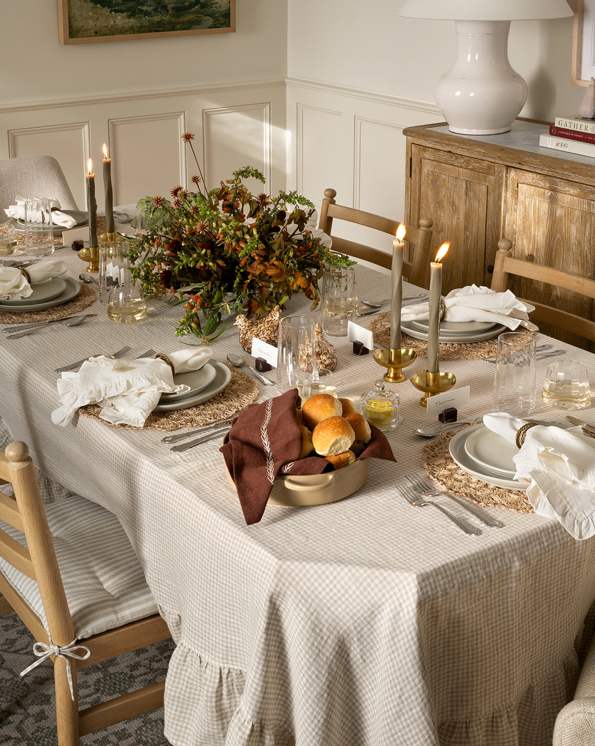 A dining table set for a meal with candles, white plates, glasses, cutlery, cloth napkins, an autumn leaf centerpiece, and dinner rolls served in the 2 Quart Stoneware Baker (Set of 2) on a beige tablecloth in a cozy, softly lit room, by McGee & Co.