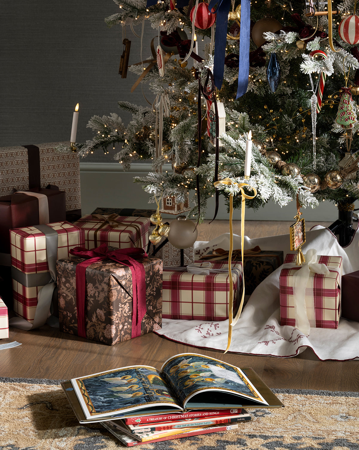 A Christmas tree with plaid and gold ornaments stands over presents wrapped in Highland Plaid Gift Wrap, while a festive book lies open on a white tree skirt in front of the gifts, by McGee & Co.