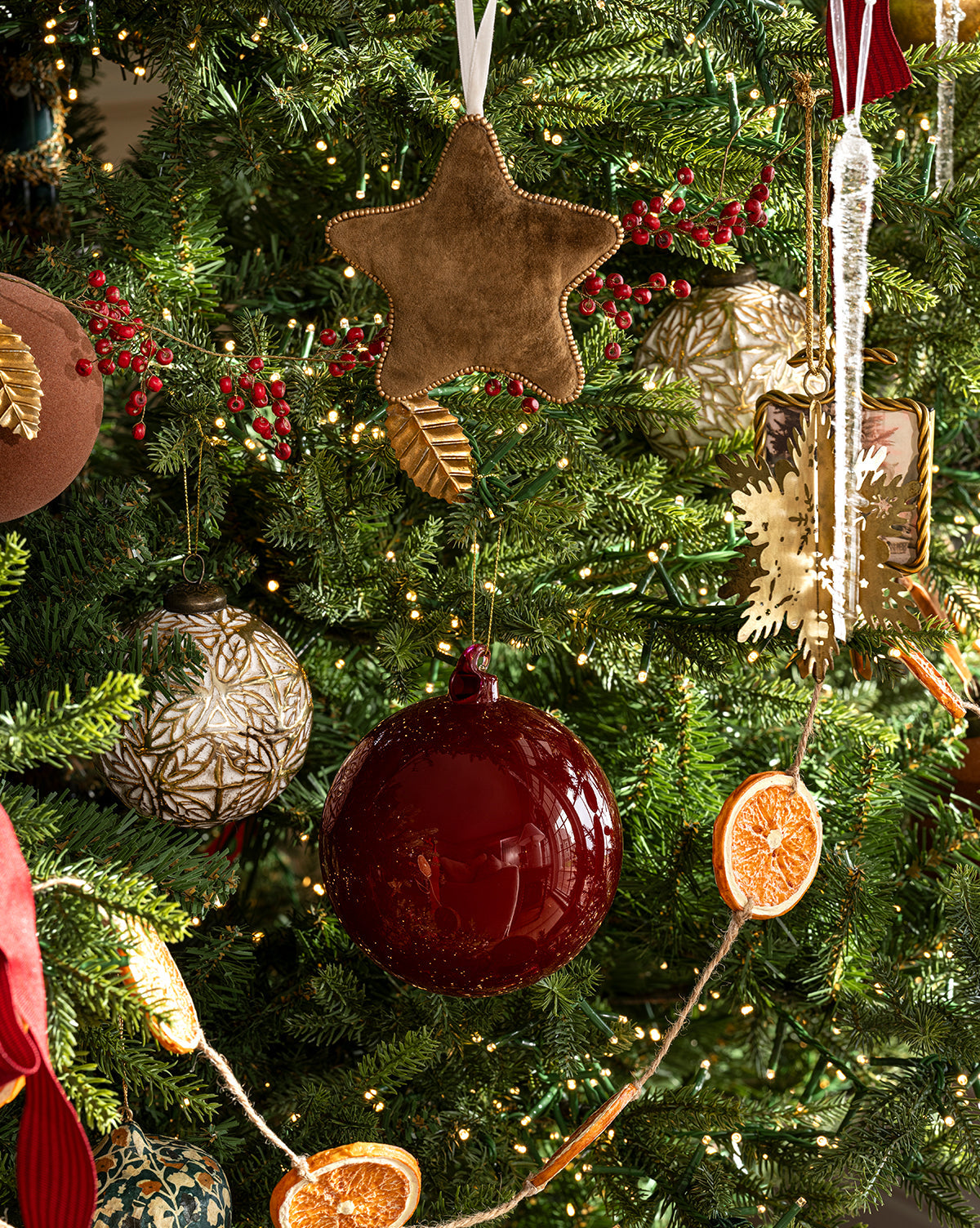 A decorated Christmas tree with ornaments like a gold star, 4" High Gloss Glass Baubles (Set of 4), gold snowflake, dried orange slices, and twinkling string lights among green pine branches—perfect for holiday décor, by McGee & Co.