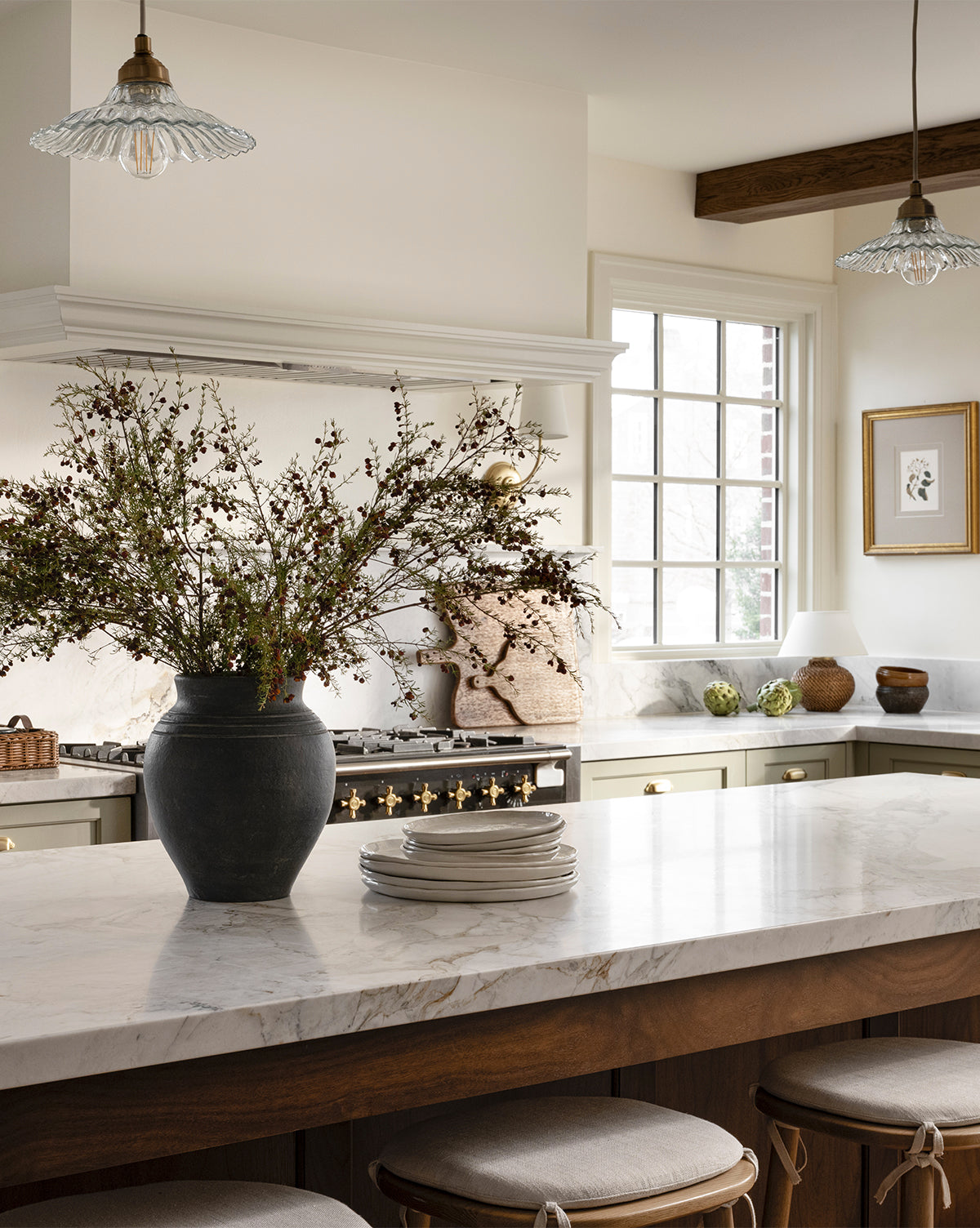A bright, elegant kitchen with a large marble island, the Ethel Vase filled with branches, stacked plates, stylish light fixtures, and a sunlit window. Warm neutrals and wood accents create a cozy rustic home decor vibe by McGee & Co.