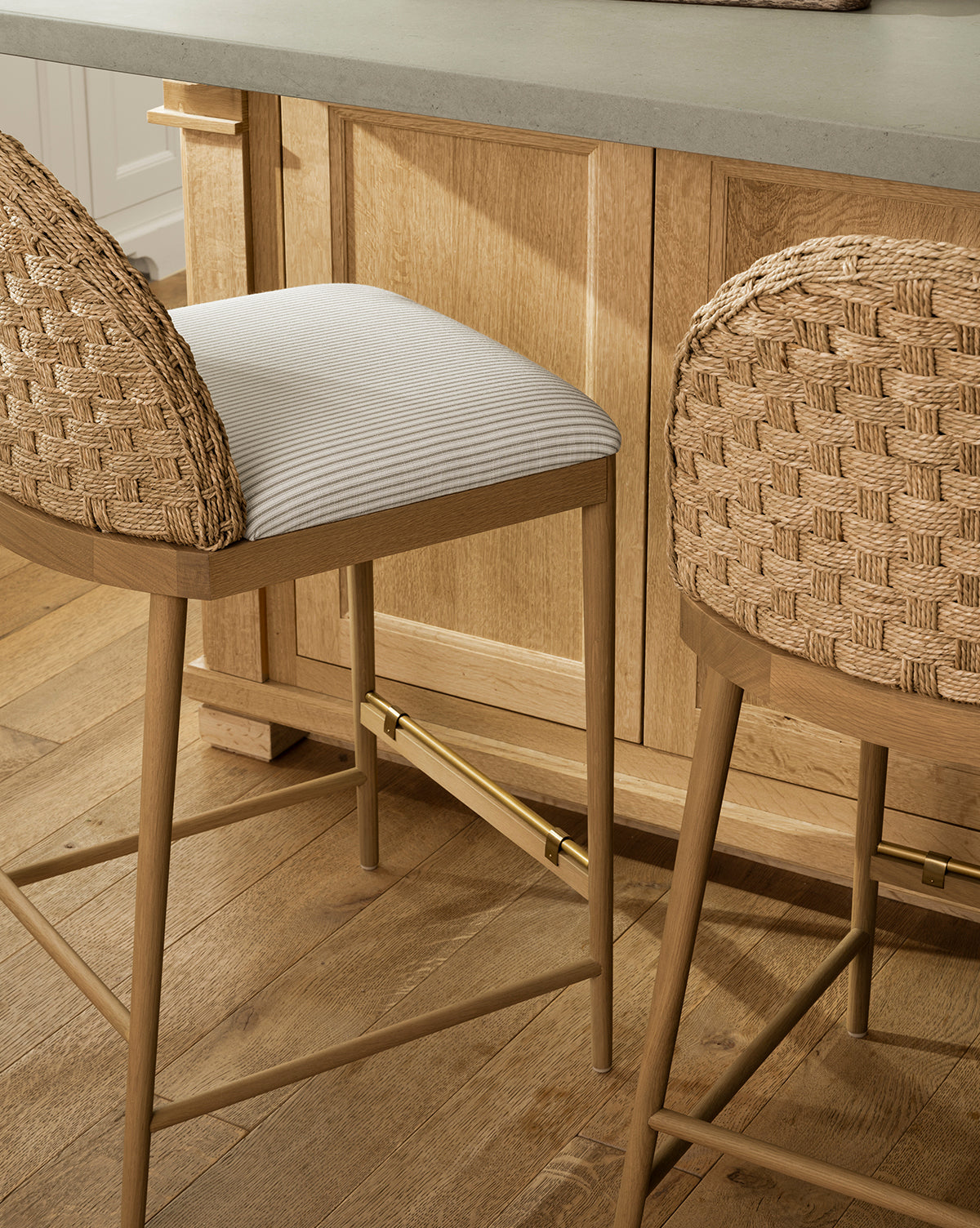 The Molly Stool in rattan woven back, solid oak legs and gold-toned footrest, with a subtle white and beige striped cushioned seat—McGee & Co.