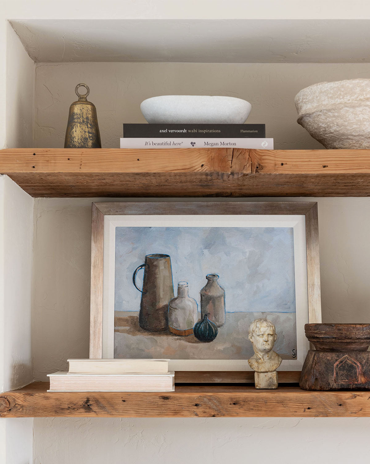 A wooden shelf holds a still-life painting, bust sculpture, stacked books, carved container, Gathered Jars, and ceramic bowls—ideal for kitchen styling or adding a decorative touch to your home against a neutral wall.