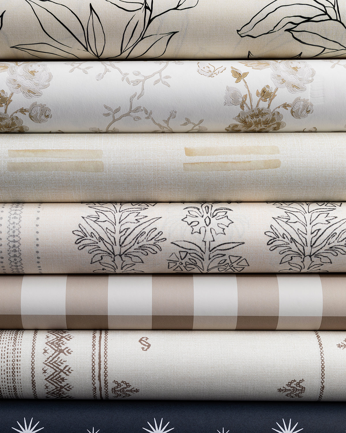 A selection of folded neutral fabrics, each with a unique pattern—florals inspired by Cecile Floral Print Wallpaper by York Wallcoverings, botanicals, stripes, checks, and geometrics—displayed against a plain background by McGee & Co.