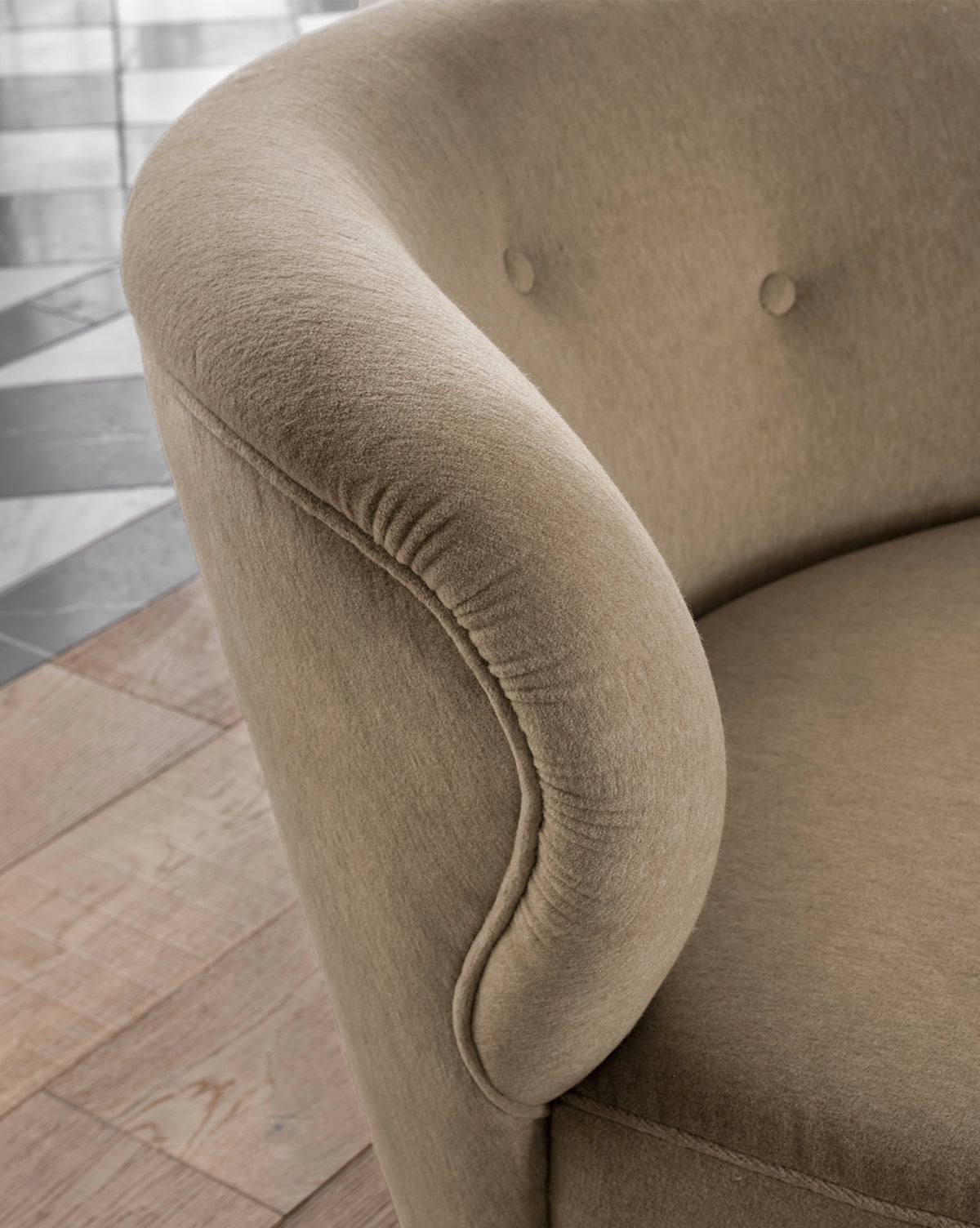 Close-up of the Carmella Slipper Chair (Ready to Ship) featuring a light brown hue, rounded arms, and button-tufted camel upholstery backrest, shown on a wooden floor with black and white tiles in the background by McGee & Co.