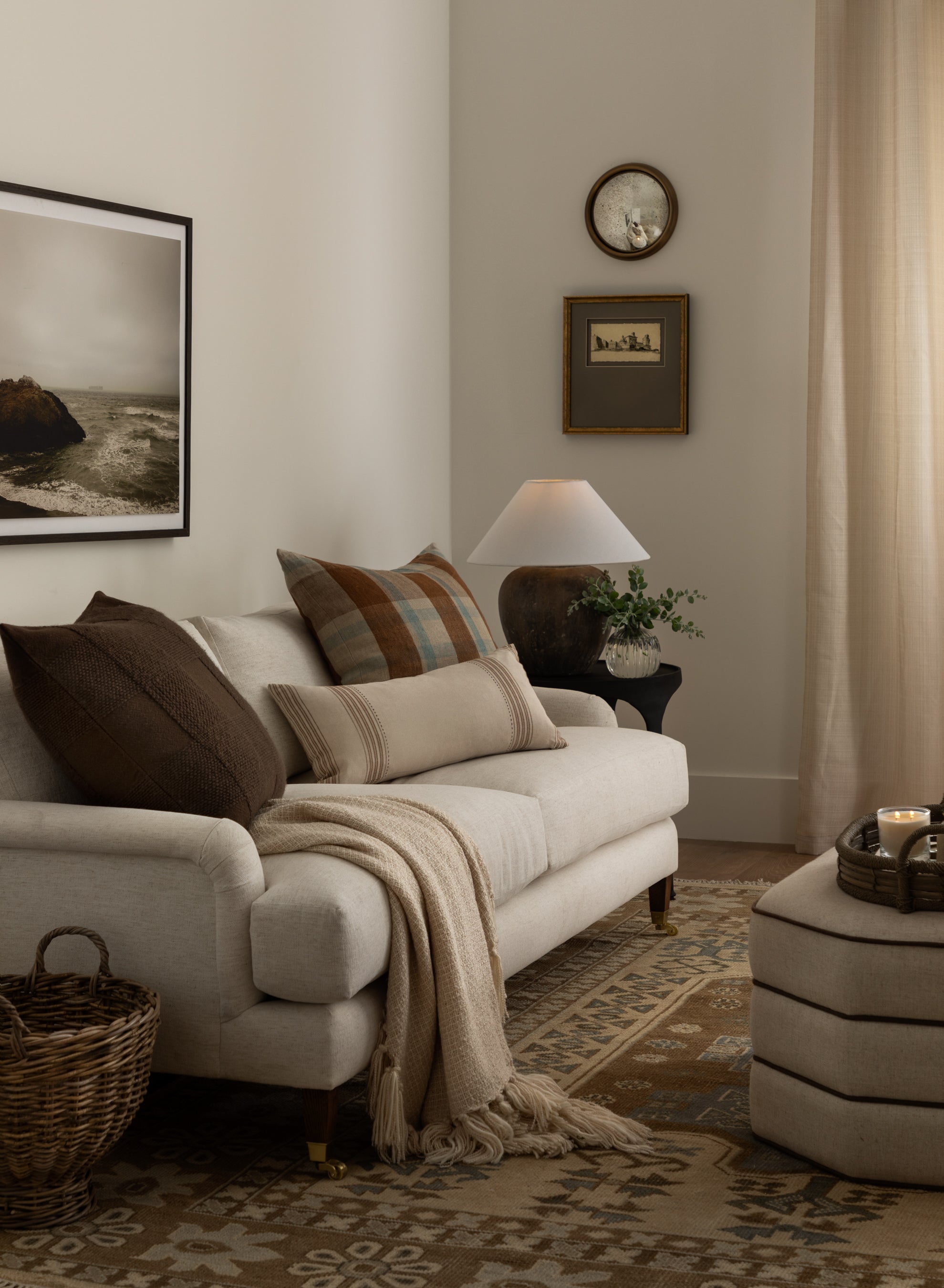 A cozy living room with a Lucille English Roll Arm Sofa 78 featuring down-wrapped cushions, earth-toned pillows, and a tan throw. A woven basket and patterned rug sit nearby, while wall art and a table lamp complete the inviting space by McGee & Co.