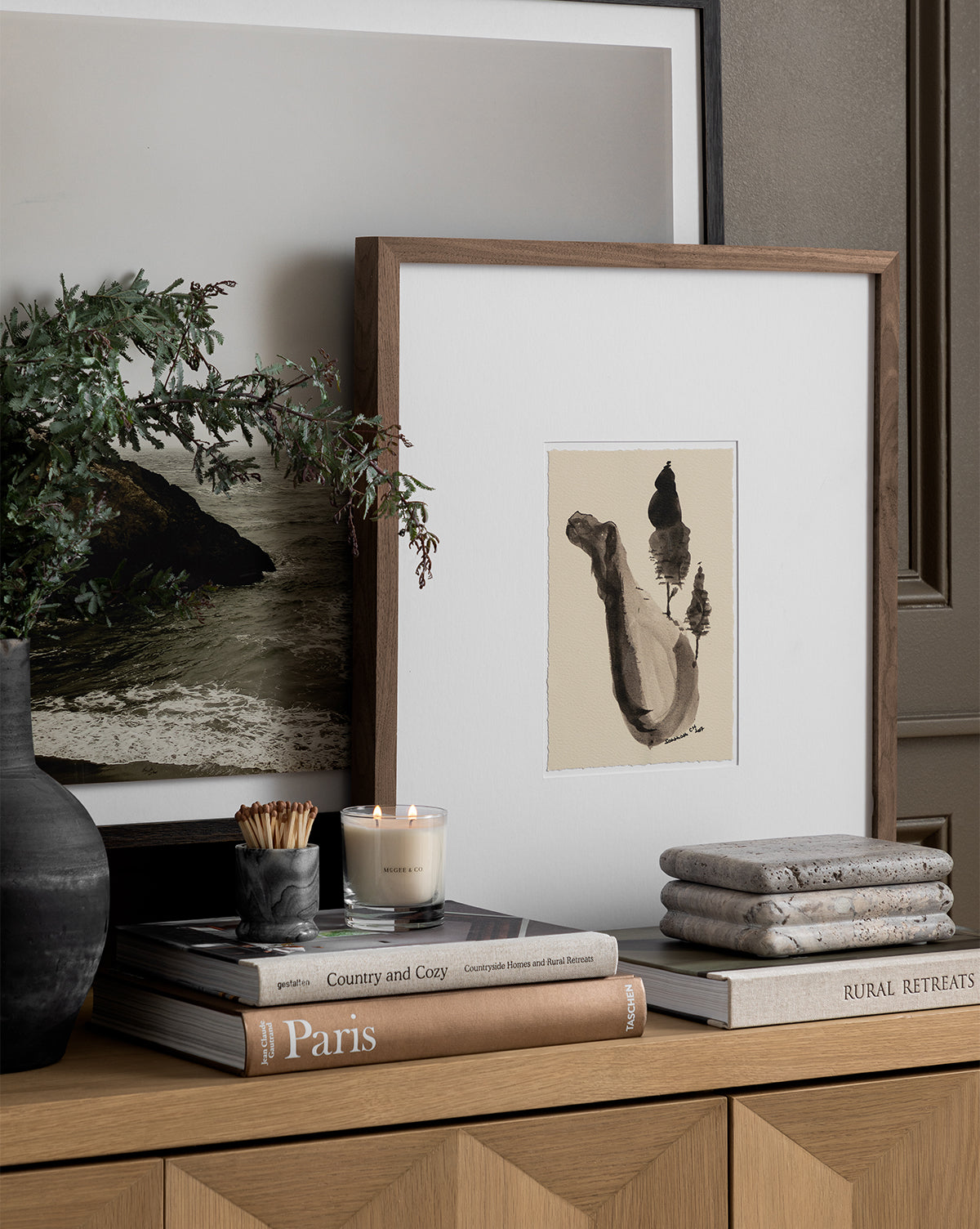 A wooden console features stacked books, a vase with greenery, art prints, a candle, matches, flat stones, and the Ives Stone Box for a cozy and elegant decor arrangement.