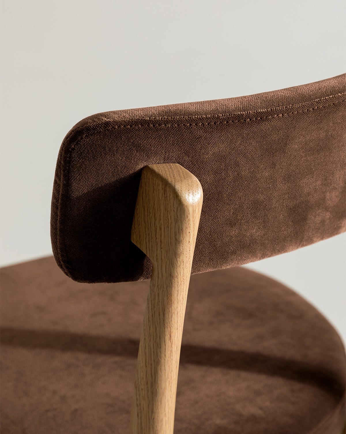 Close-up of the Garance Dining Chair, showcasing its modern design with a brown suede-like upholstered backrest and seat, connected by a curved white oak support, by McGee & Co.