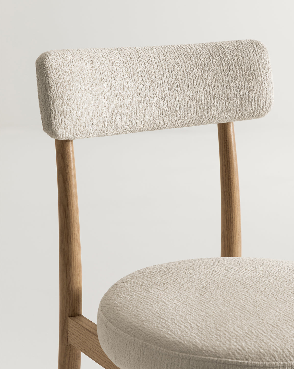 The Garance Dining Chair features a modern light wood frame, a round cushioned seat, and a rectangular backrest in textured off-white fabric, all set against a plain light background, by McGee & Co.
