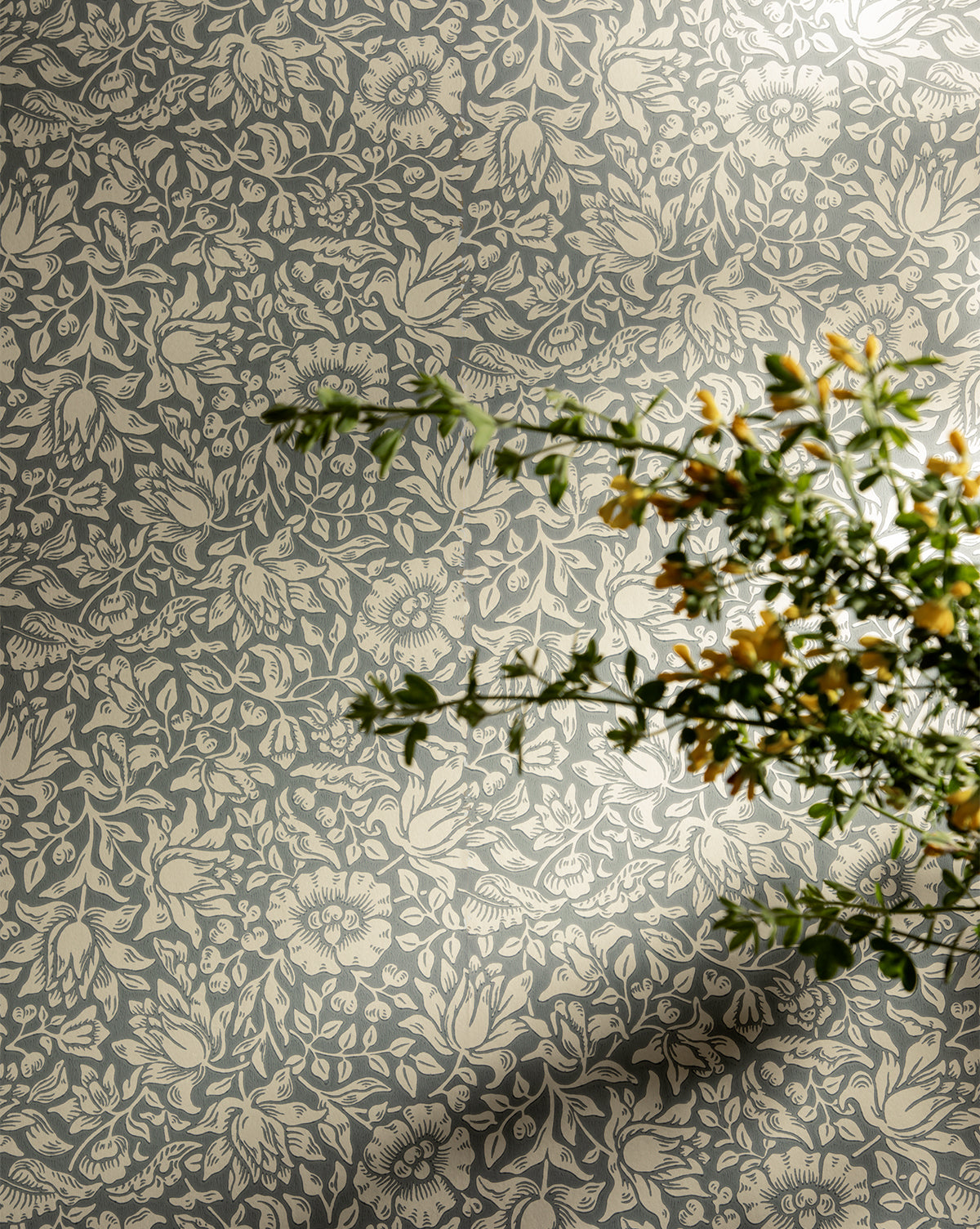 Certainly! Here’s your revised sentence with the exact string McGee & Co. blended at the end: A leafy green plant with small yellow flowers casts a shadow on the Morris & Co. x McGee & Co. Mallow Wallpaper by Sanderson Design Group, Inc., which features a light floral and leafy design on a muted blue-gray background, McGee & Co.
