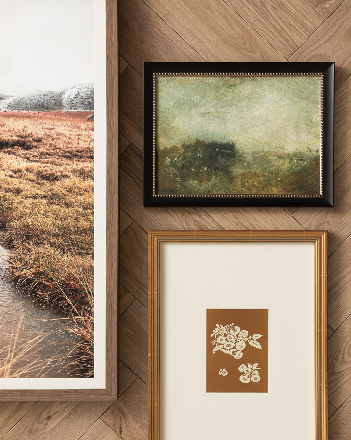 Three framed wall art pieces—Lace Detail, a gold floral illustration with a lace pattern, plus a landscape photograph of grassy marsh and a green abstract in black frame—enhance the herringbone wood wall. Perfect for home decor, by McGee & Co.