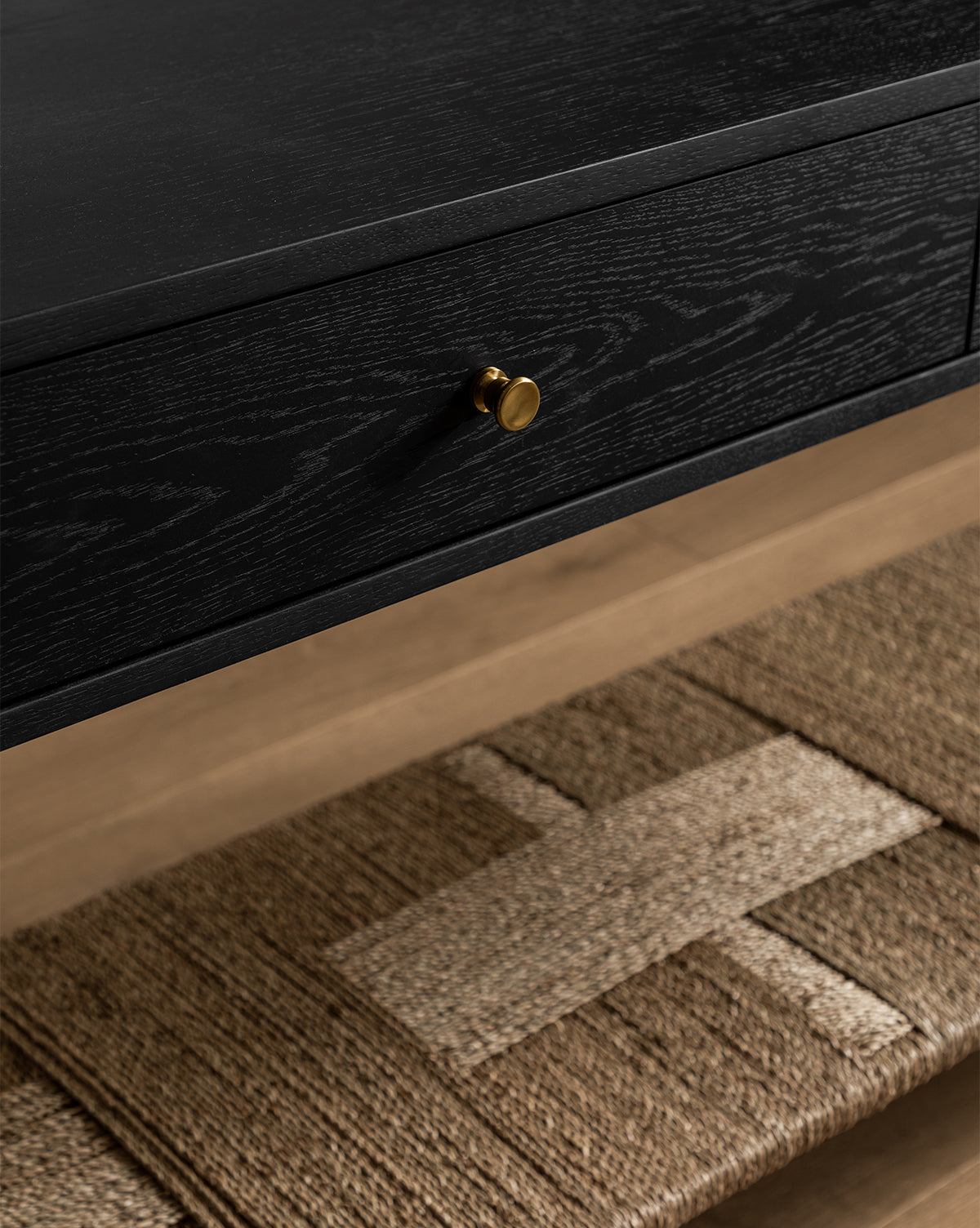 Close-up of the Dana Consoles oak drawer with brass hardware, set above a geometric woven rug on a wooden floor—ideal for adding stylish flair to your entryway, by McGee & Co.