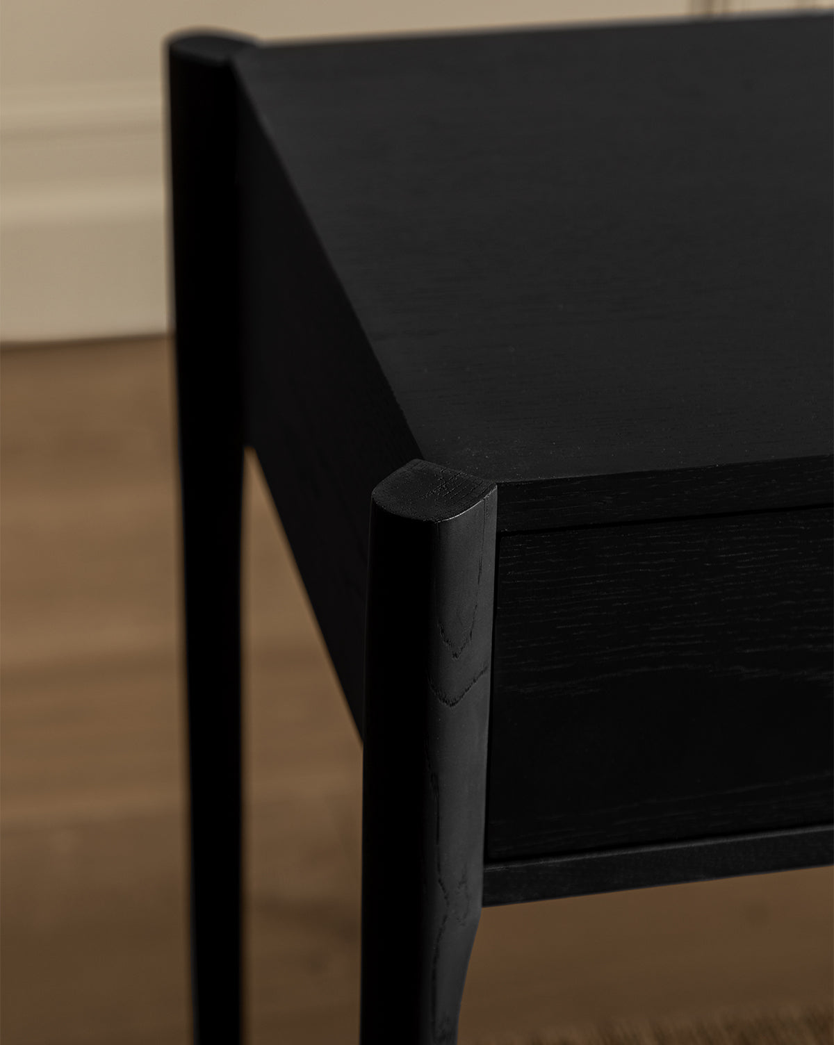 Close-up of the Dana Console in modern black oak with straight legs, set on a light wooden floor. The slightly blurred background features a beige wall with molding, making it ideal for stylish entryway decor, by McGee & Co.